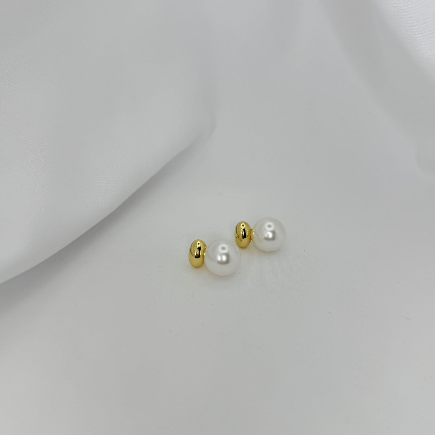 Pair of pearl earrings with gold accents on a light gray background