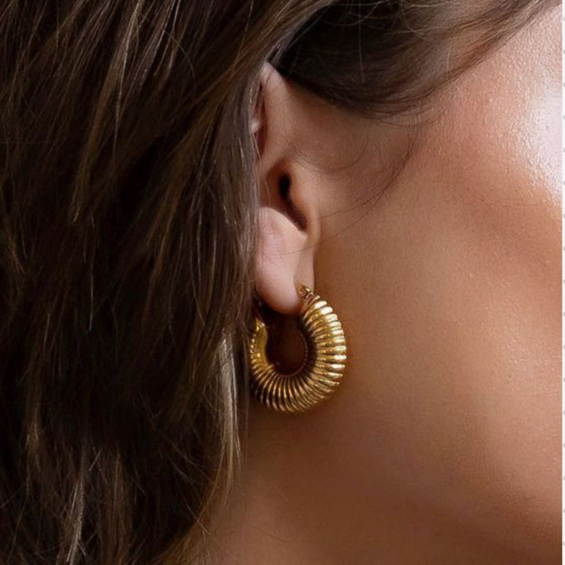 Close-up of a person wearing gold hoop earrings with hair partially covering the face.