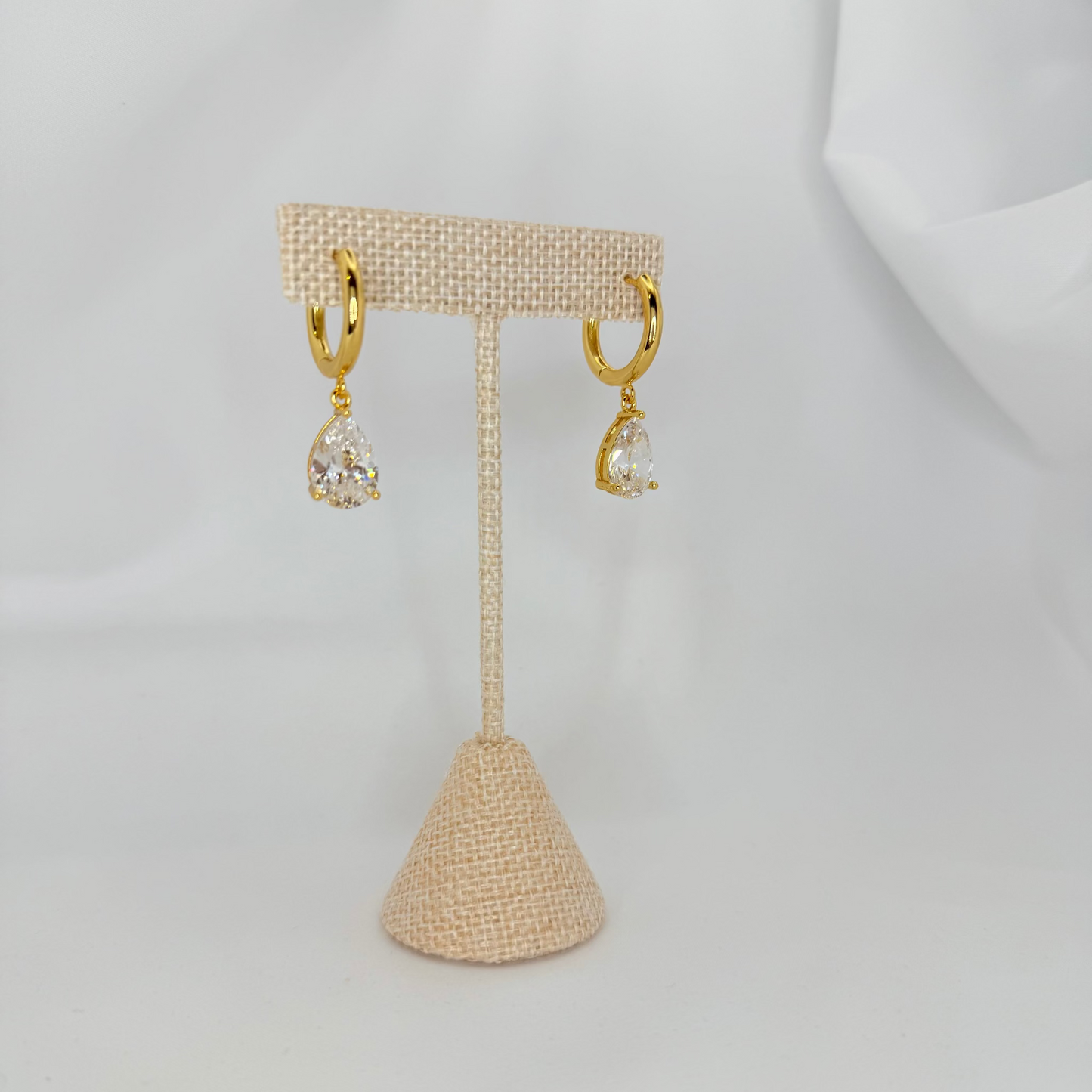 Gold earrings on a beige earring stand against a white background