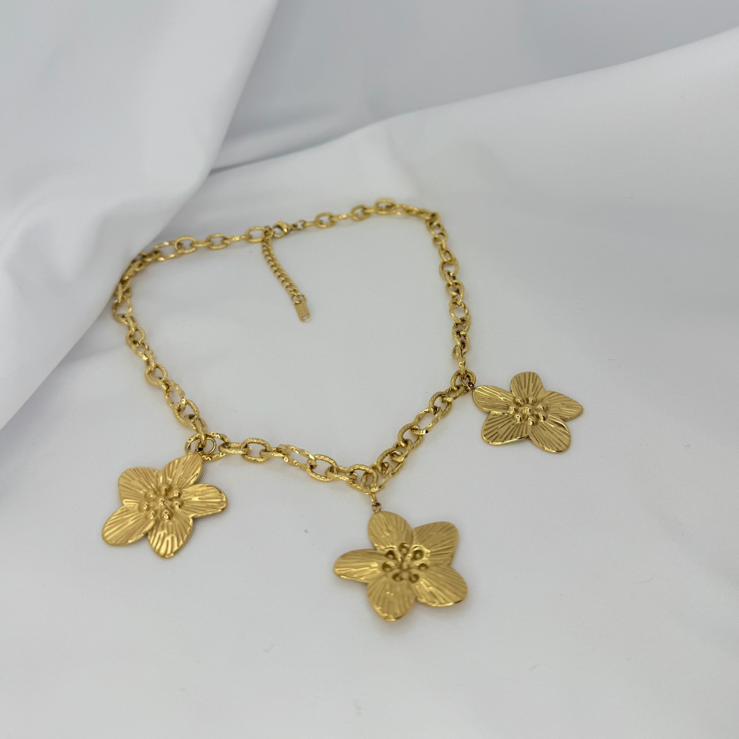 Gold necklace with floral pendants on a white fabric background