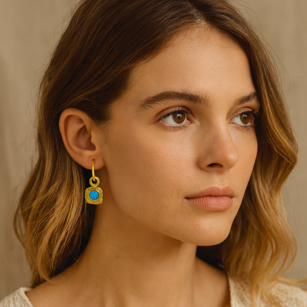 Woman wearing gold earrings with a blue gemstone against a beige background