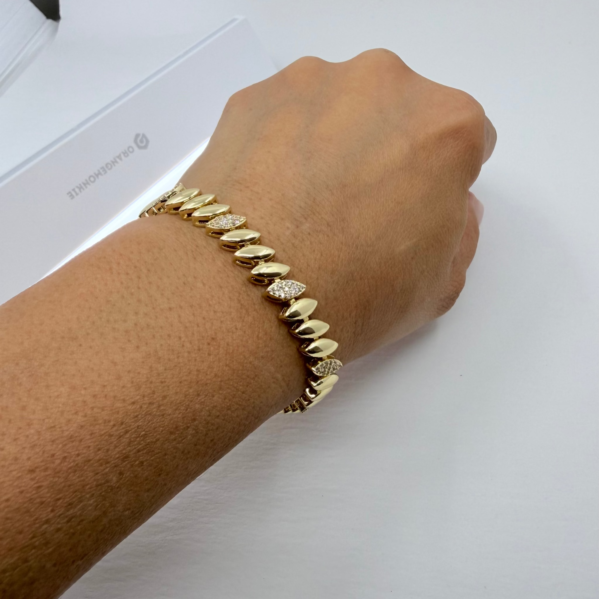 A gold chain bracelet with a textured, spiked design and a small clear crystal accent