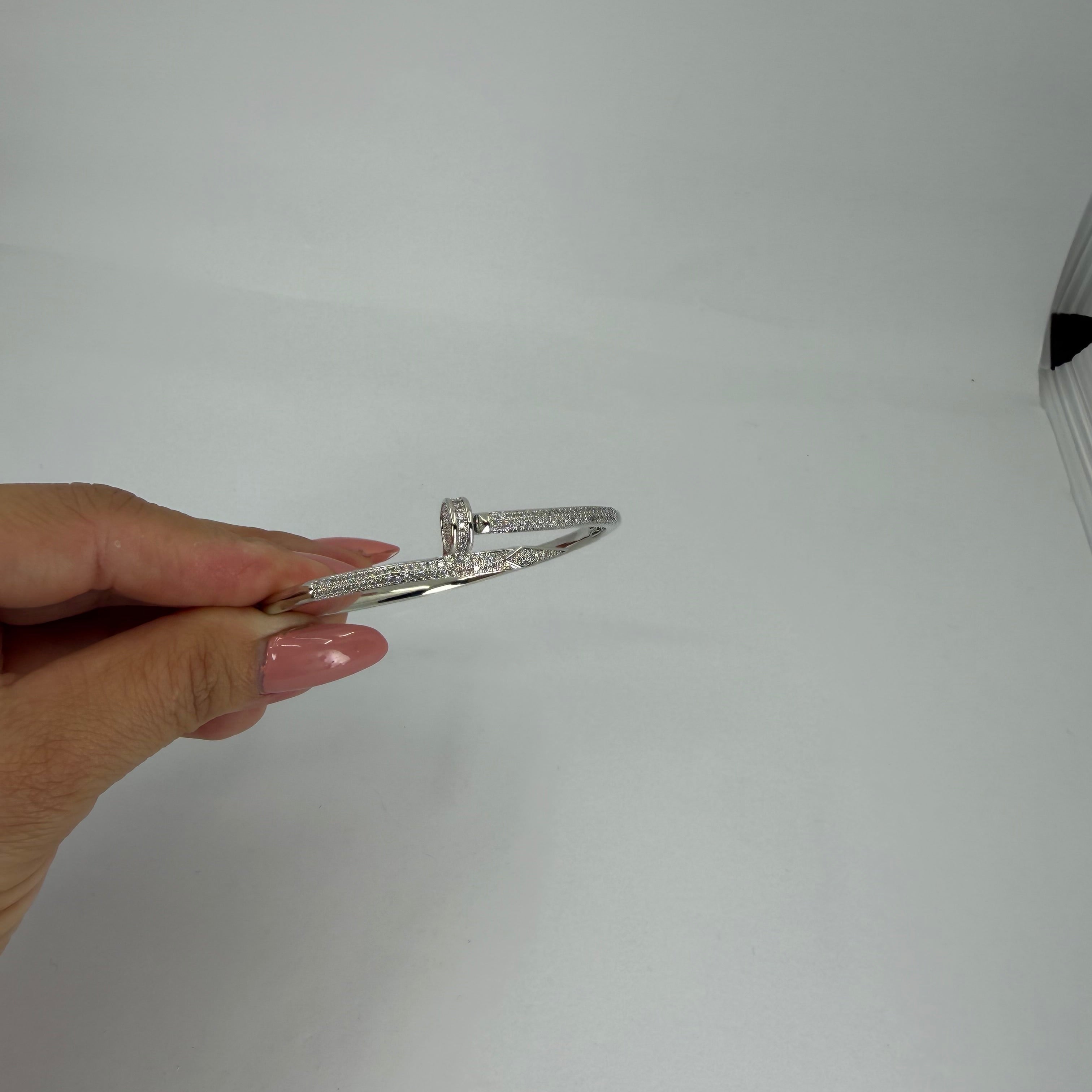 Hand holding a silver bracelet against a white background