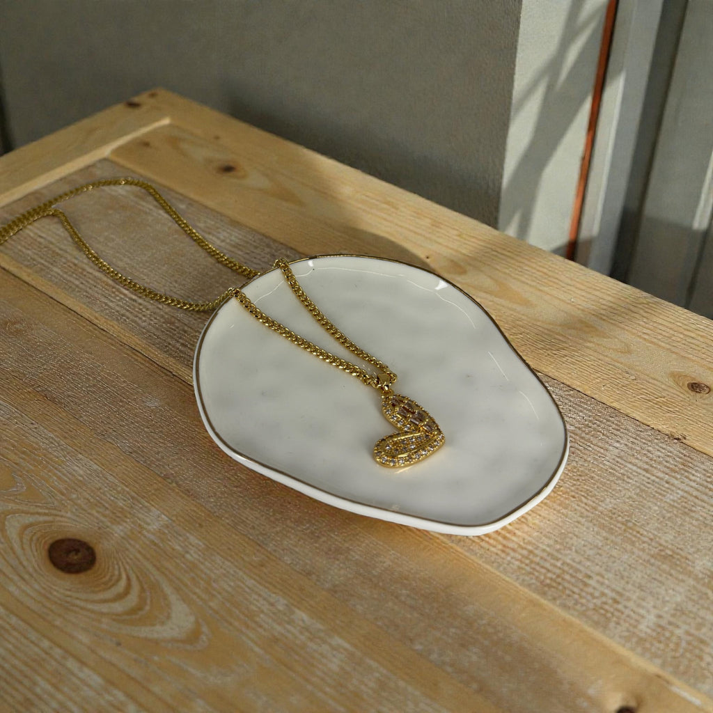 Gold necklace with a heart pendant on a white dish on a wooden surface