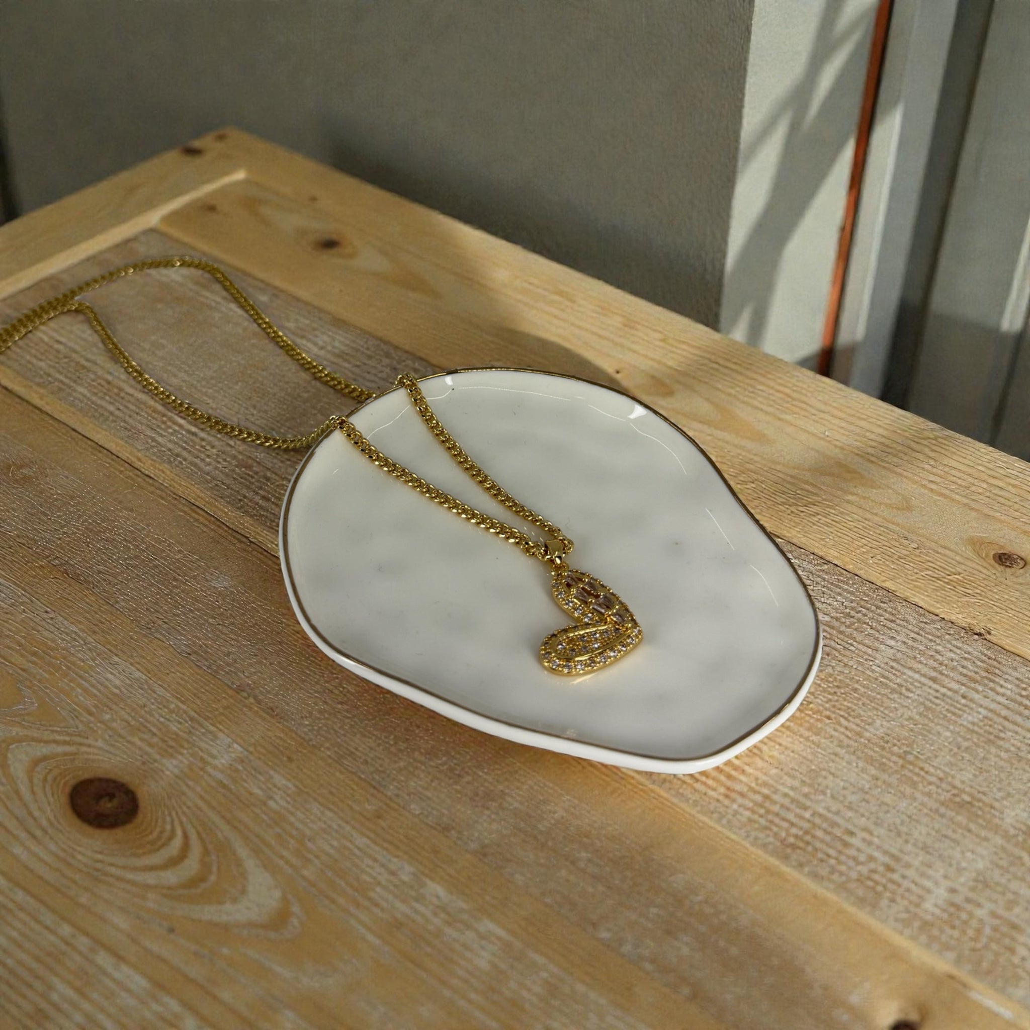 Gold necklace with a heart pendant on a white dish on a wooden surface