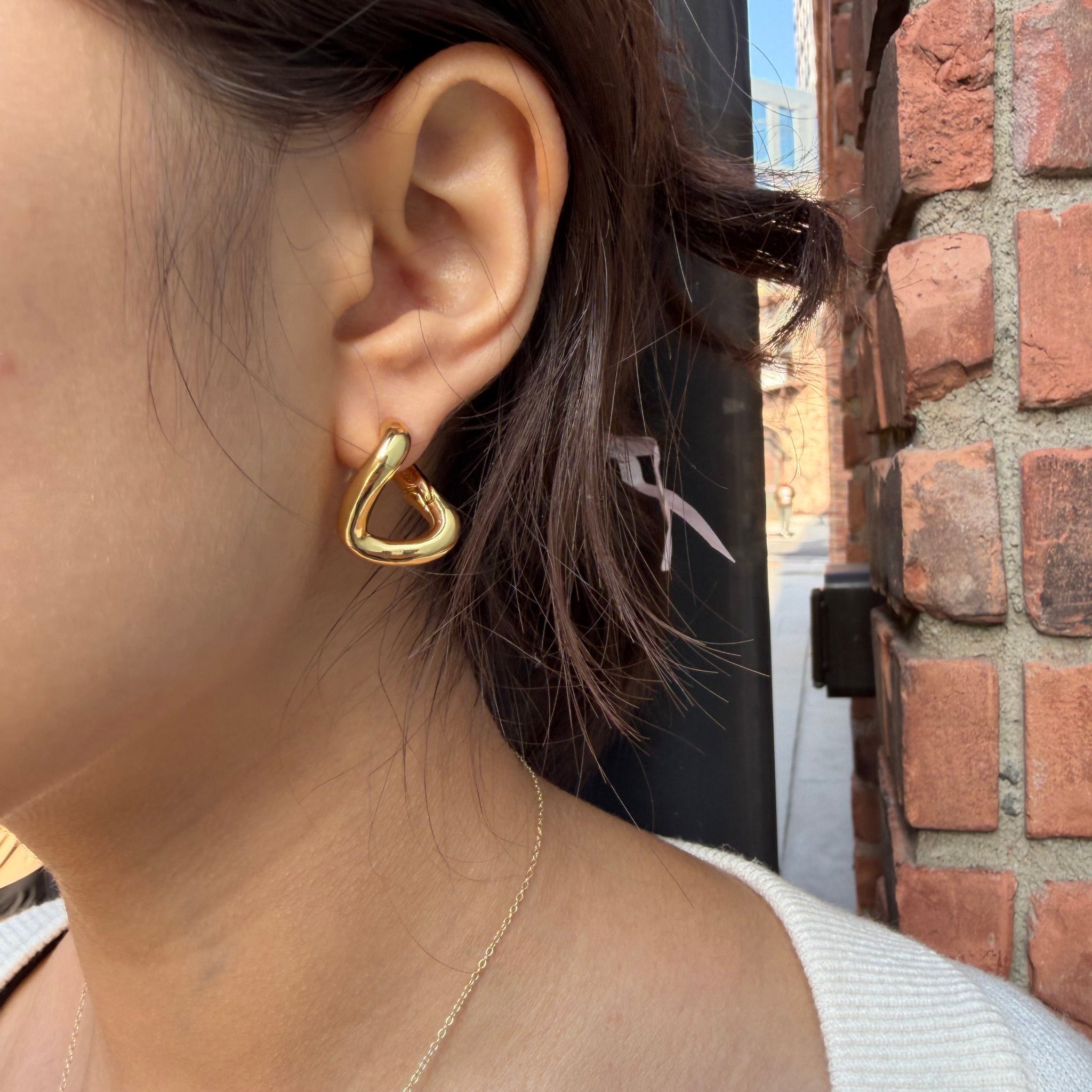 Close-up of an ear wearing a gold heart-shaped earring against a brick wall background.
