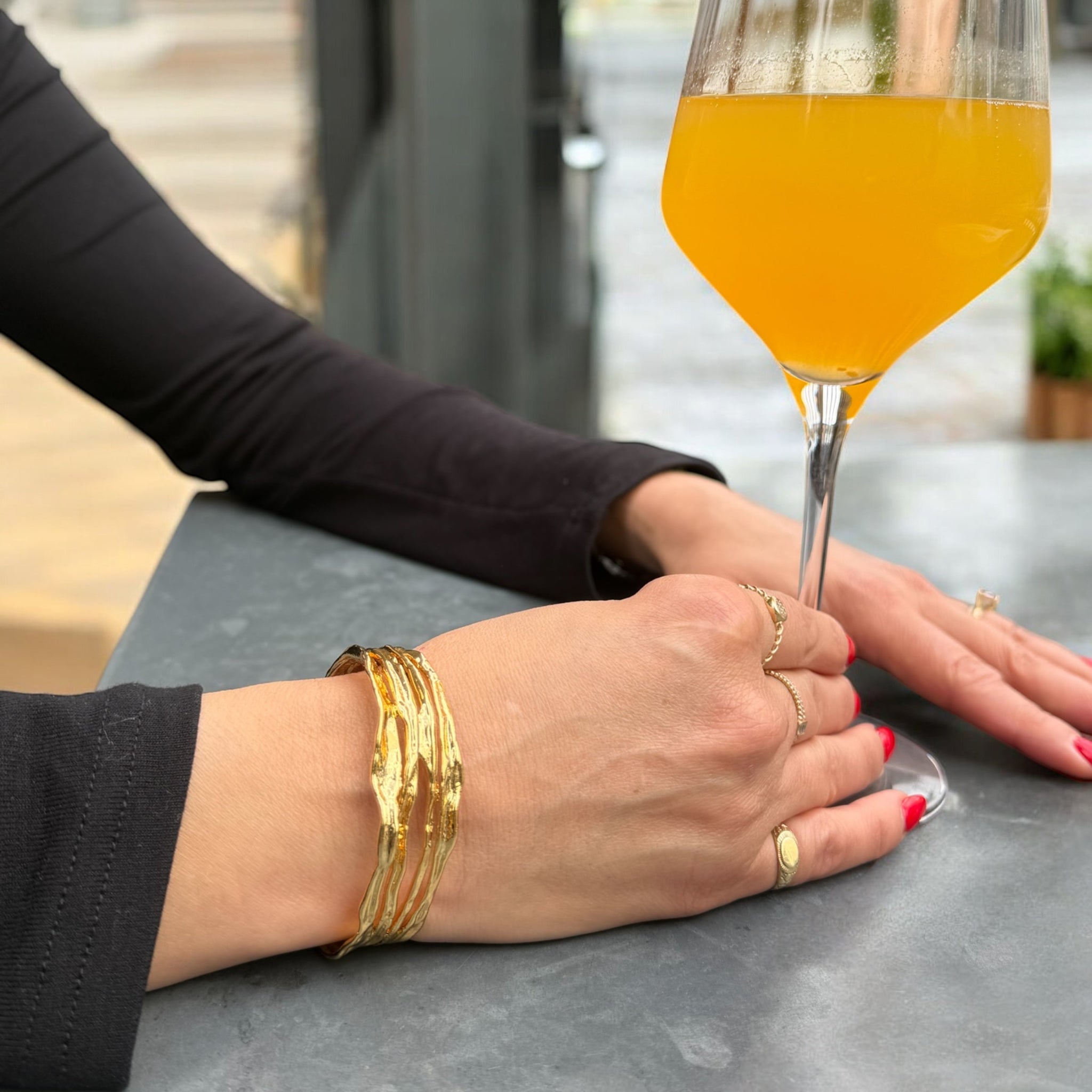 Close-up of hands with gold bracelets and rings, holding a glass of orange juice.