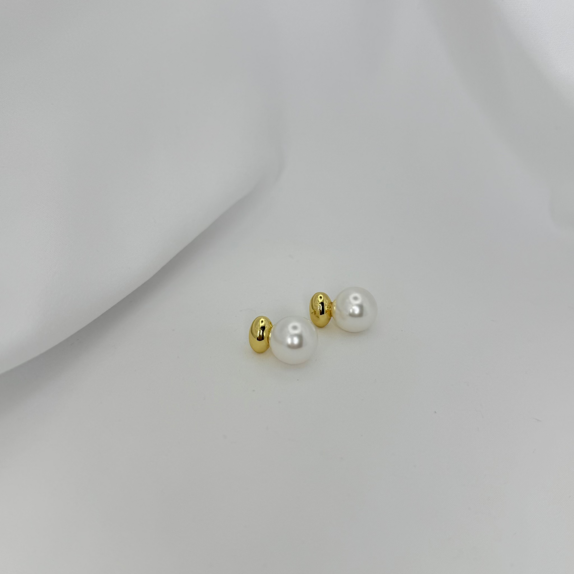Pair of pearl earrings with gold accents on a light gray background