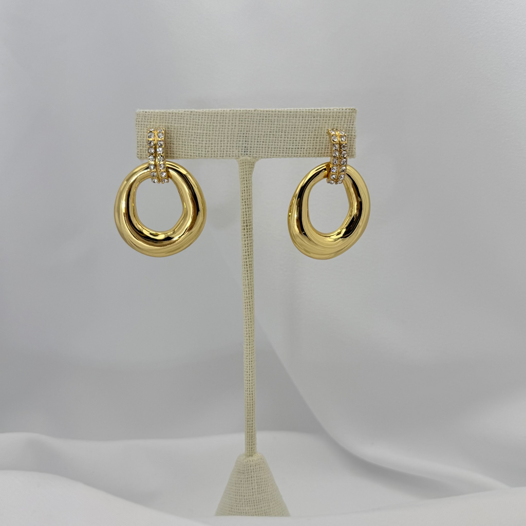 Gold hoop earrings on a beige earring stand against a light gray background