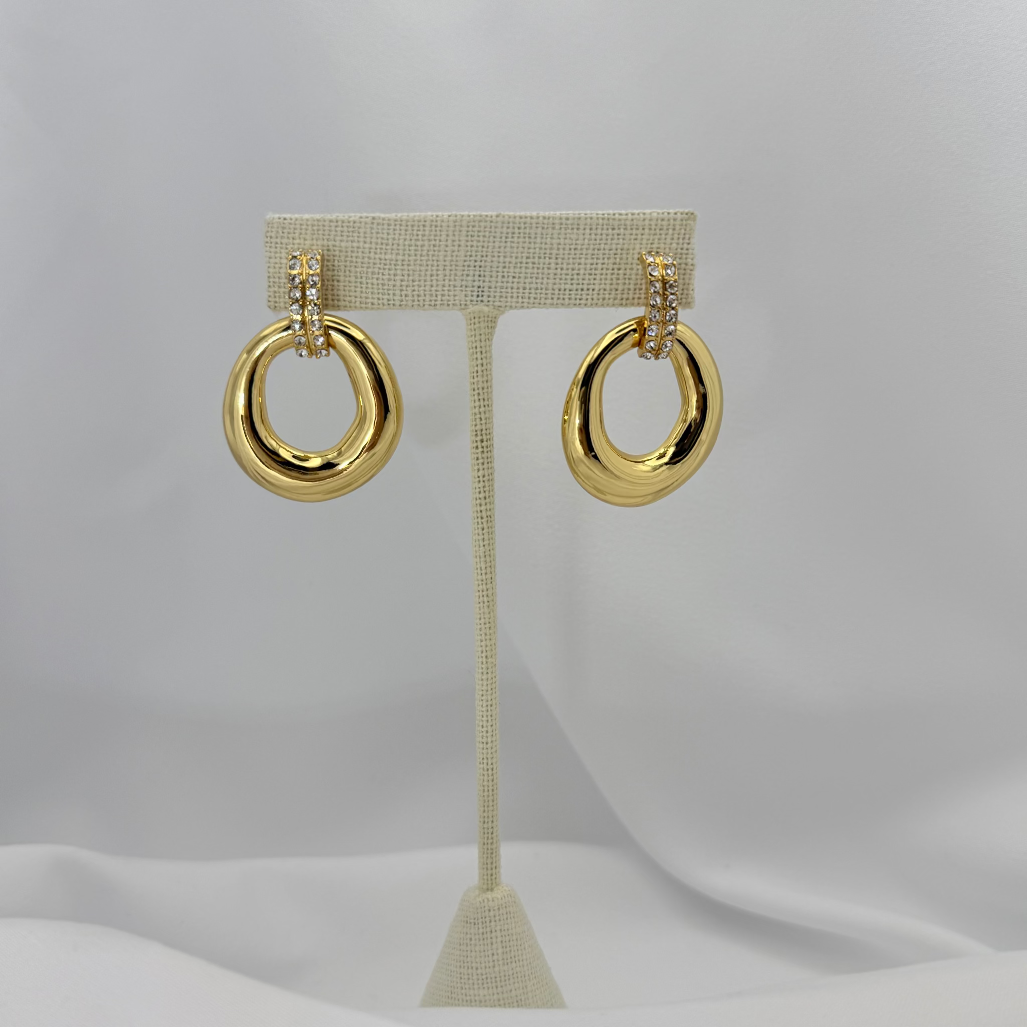 Gold hoop earrings on a beige earring stand against a light gray background