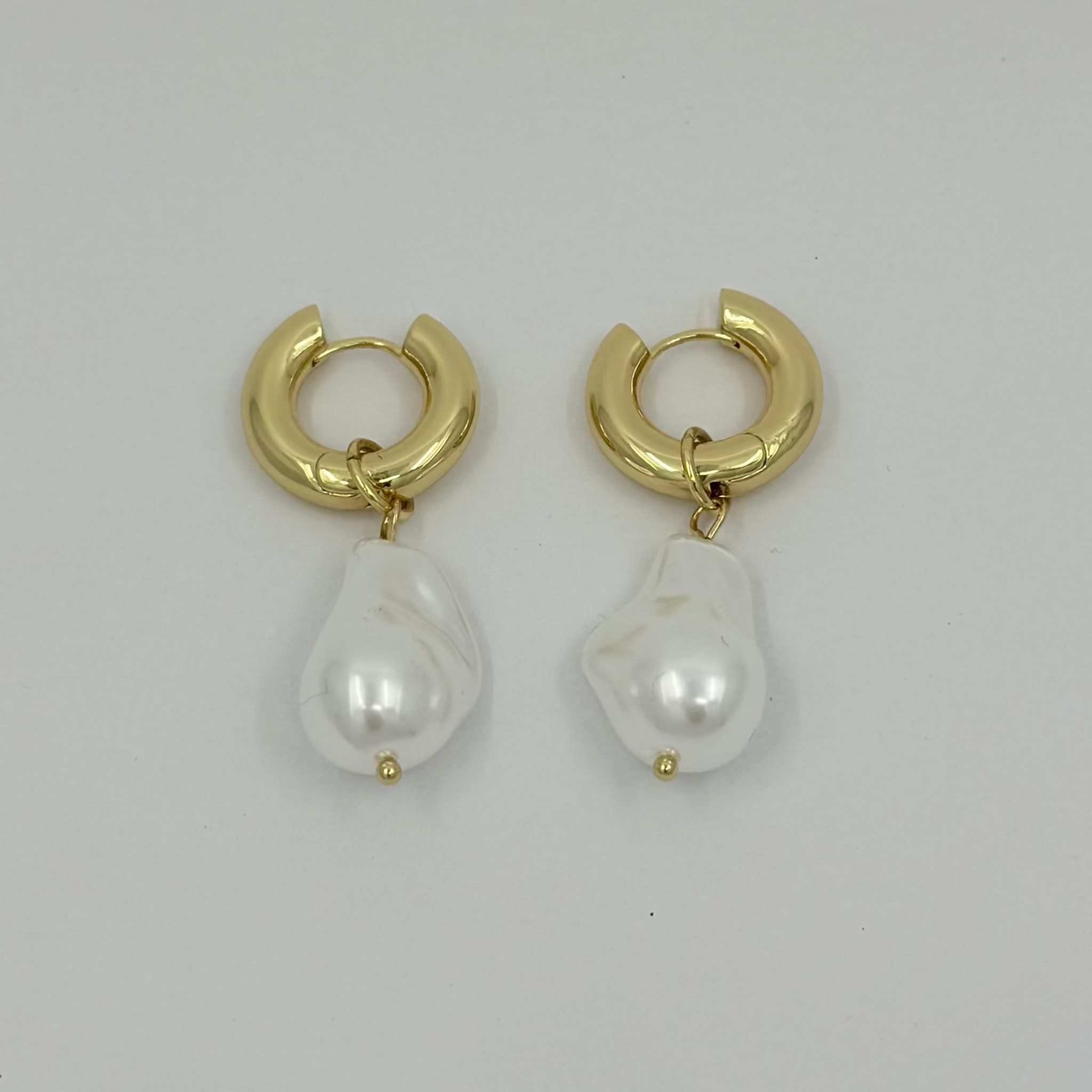 Gold hoop earrings with pearl drops on a light gray background