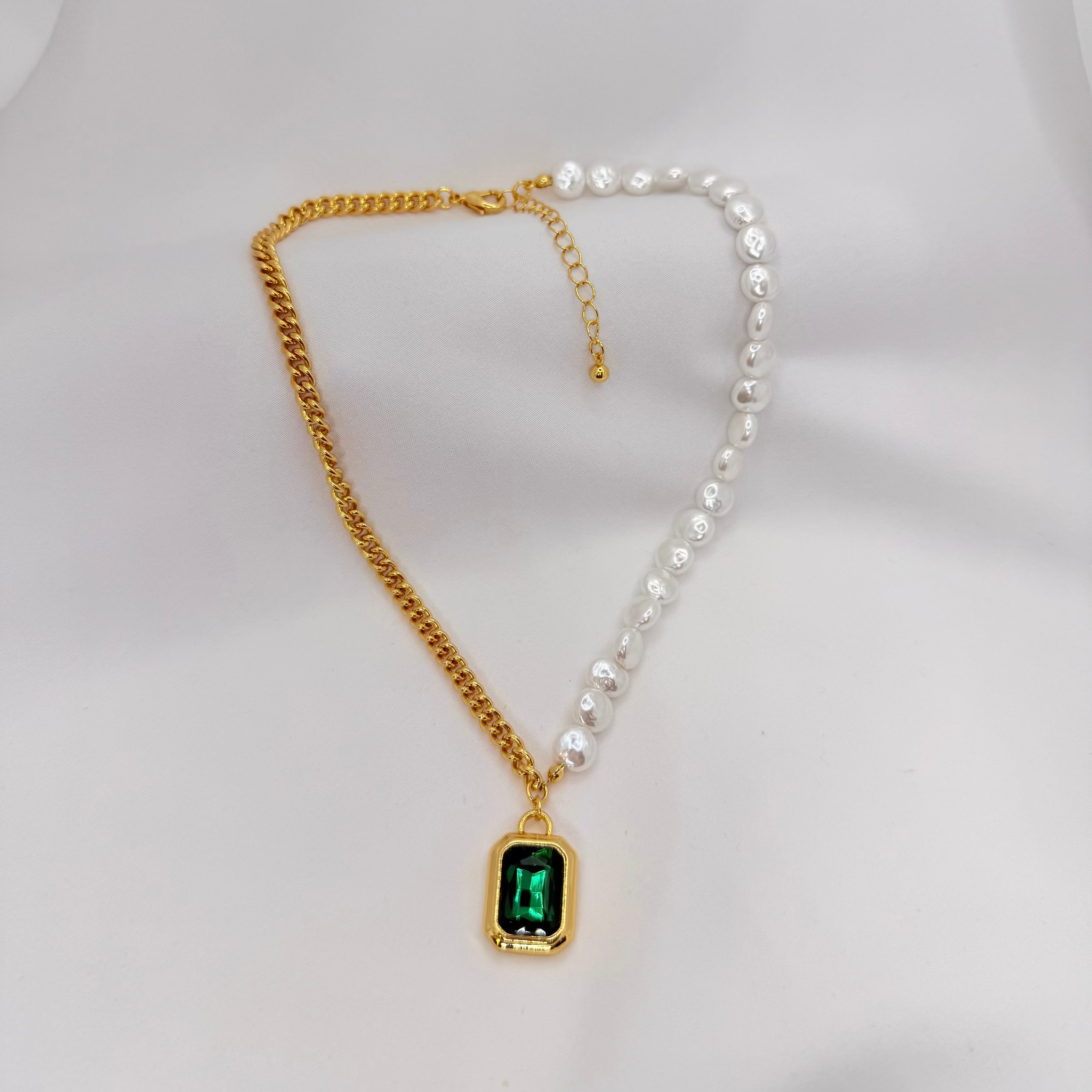 Gold chain necklace with a green gemstone pendant on a white background