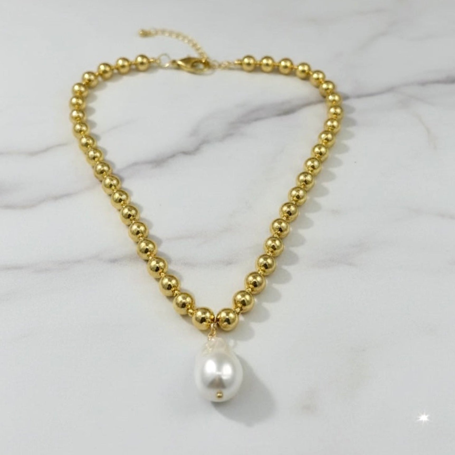 Gold beaded necklace with a pearl pendant on a marble surface