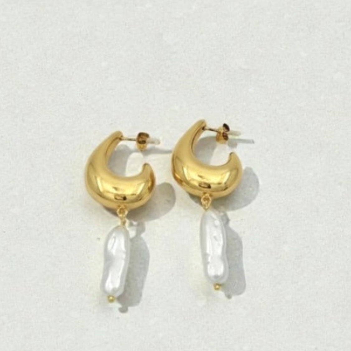 Gold earrings with moon designs and pearl-like beads on a light gray background