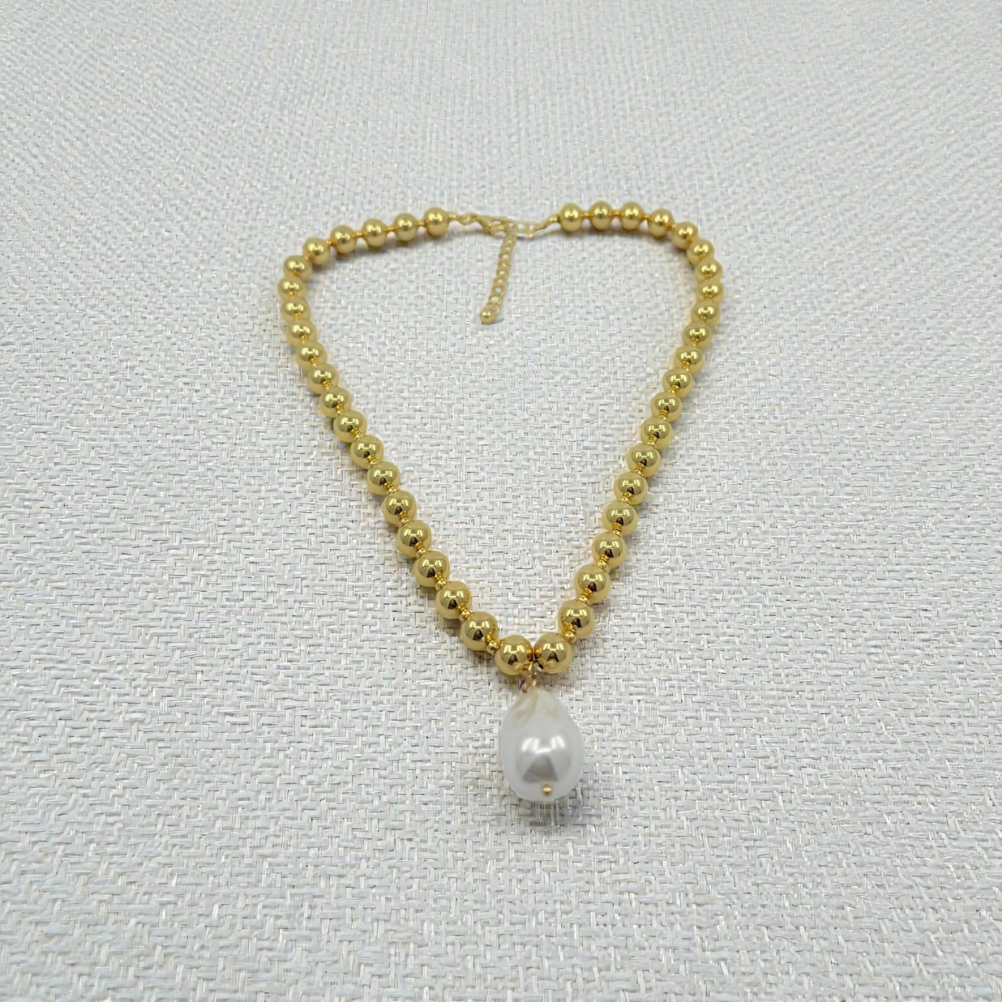 Gold beaded necklace with a single pearl pendant on a light gray background