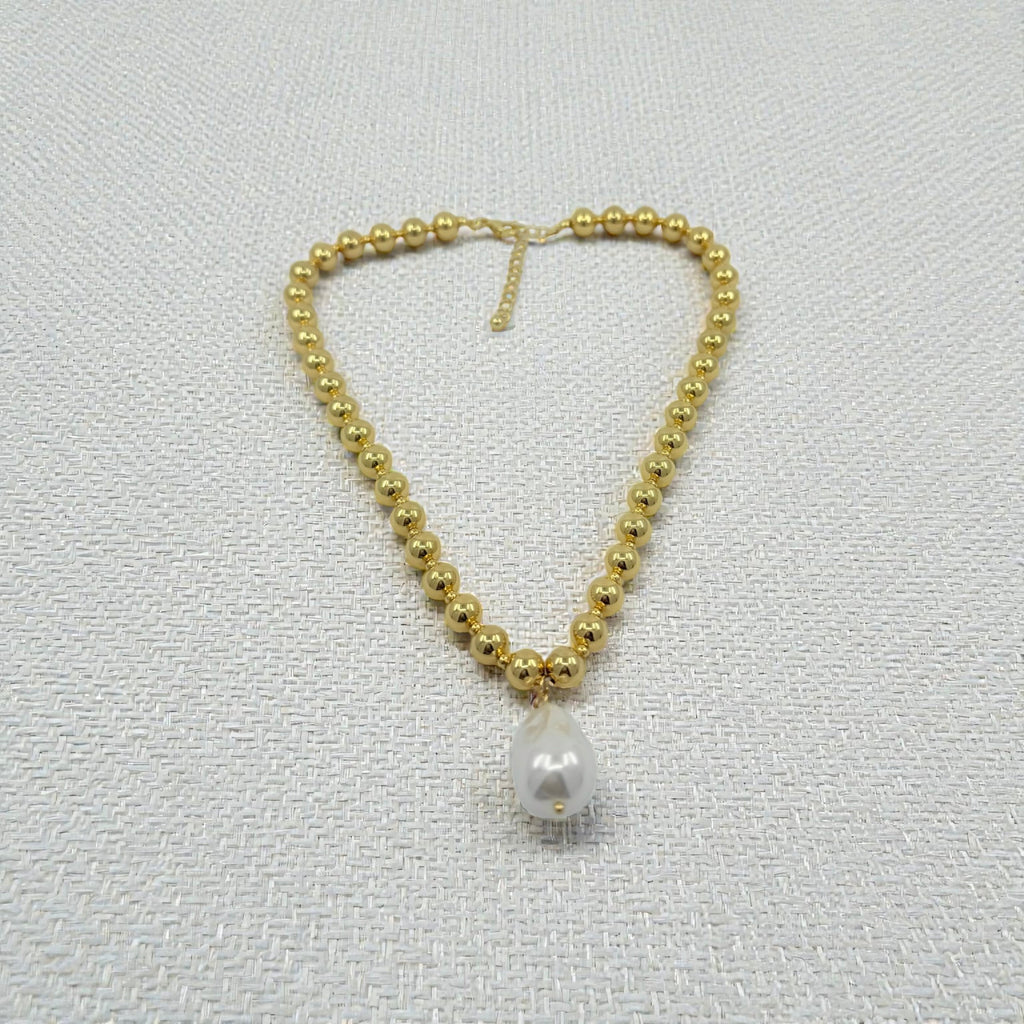 Gold beaded necklace with a single pearl pendant on a light gray background