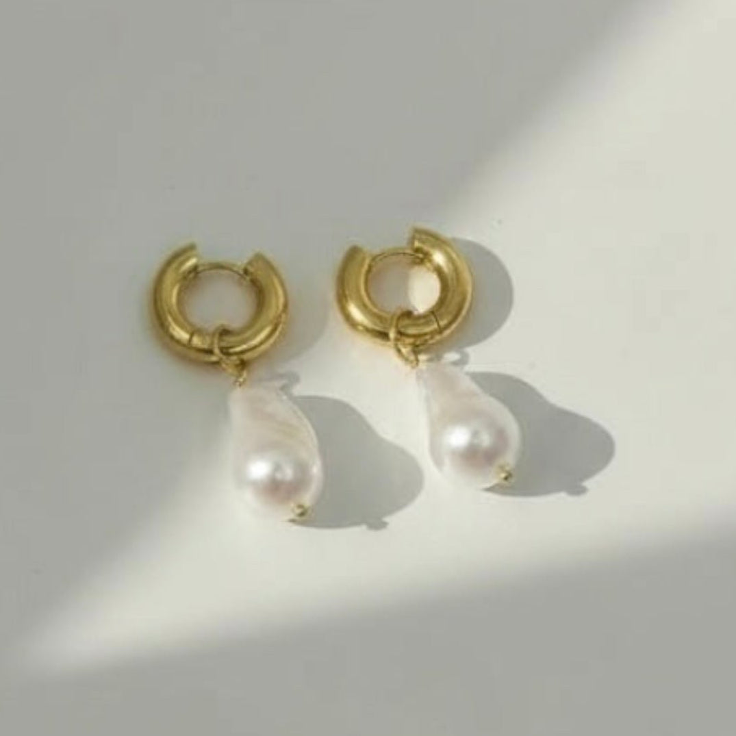 Gold hoop earrings with pearl drops on a light gray background