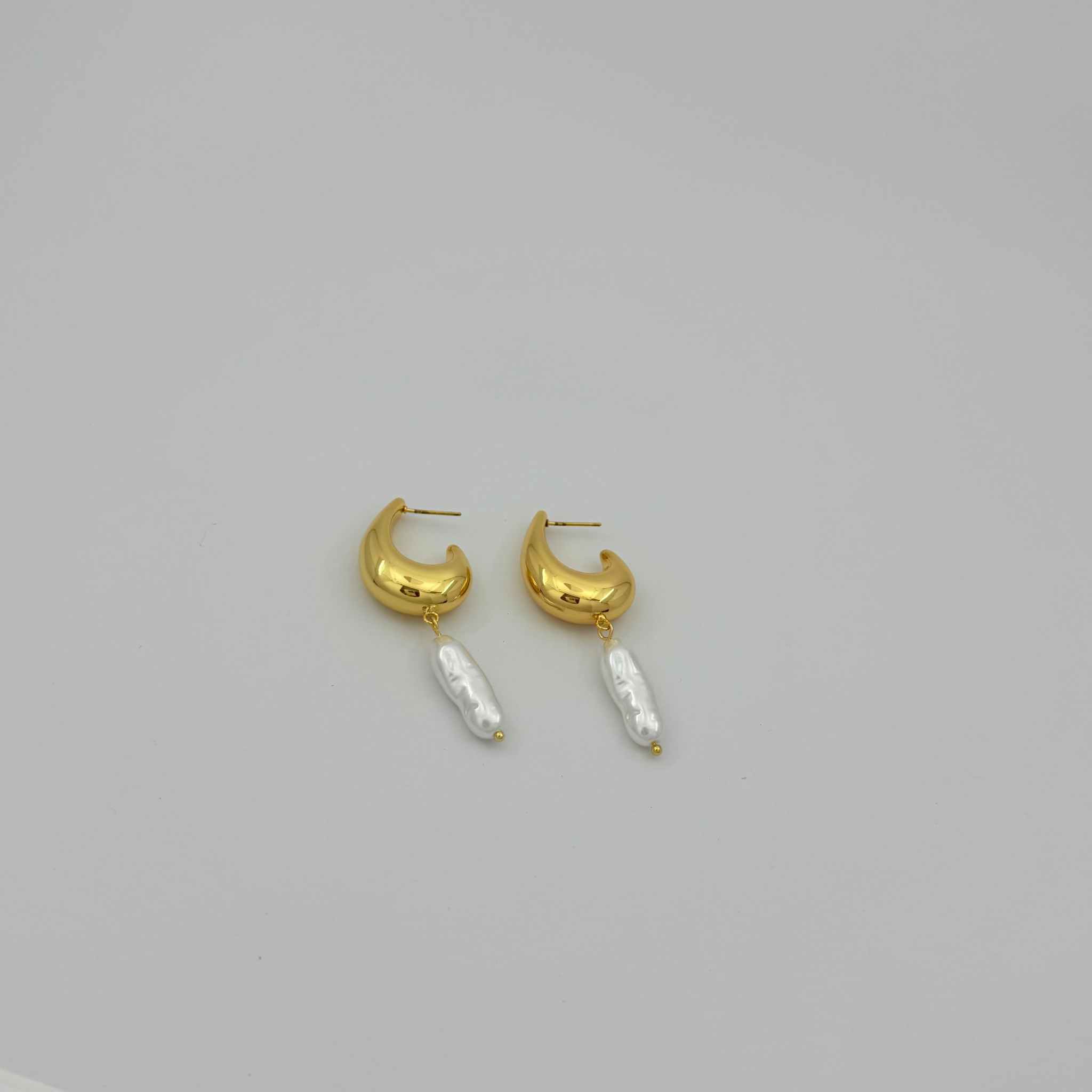 Gold hoop earrings with pearl-like beads on a light gray background