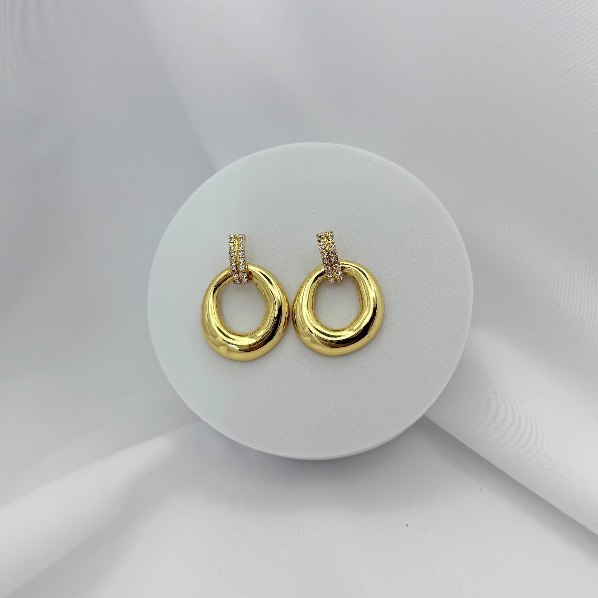 Gold hoop earrings on a white circular stand with a light gray background