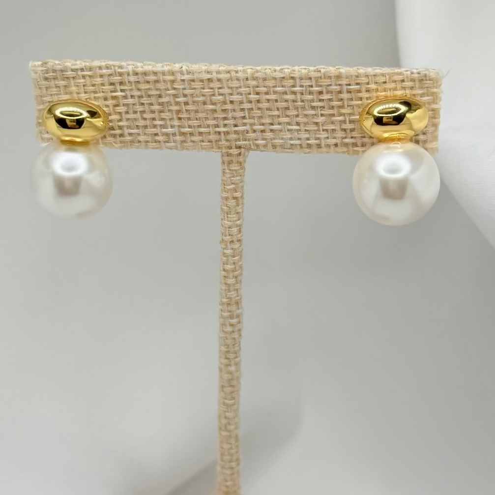 Pair of pearl earrings on a beige stand against a white background