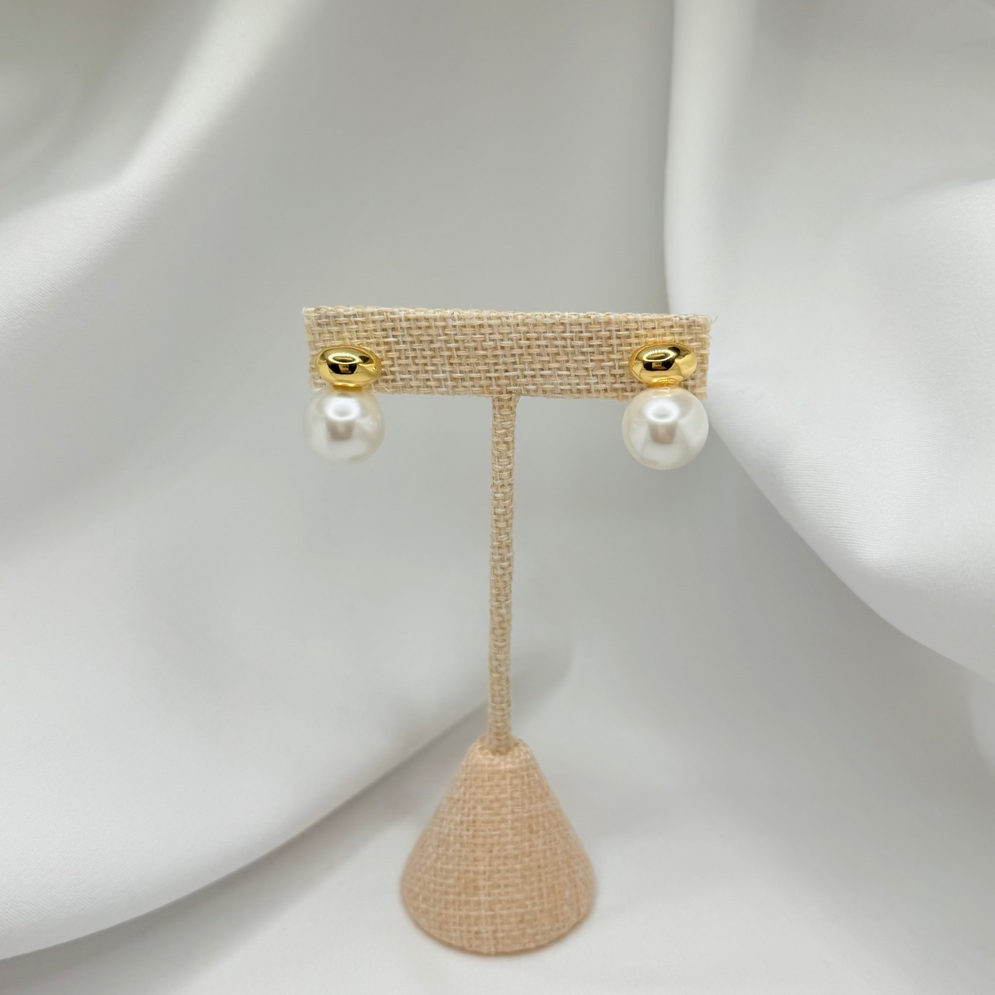 Pair of pearl earrings on a beige stand against a white background