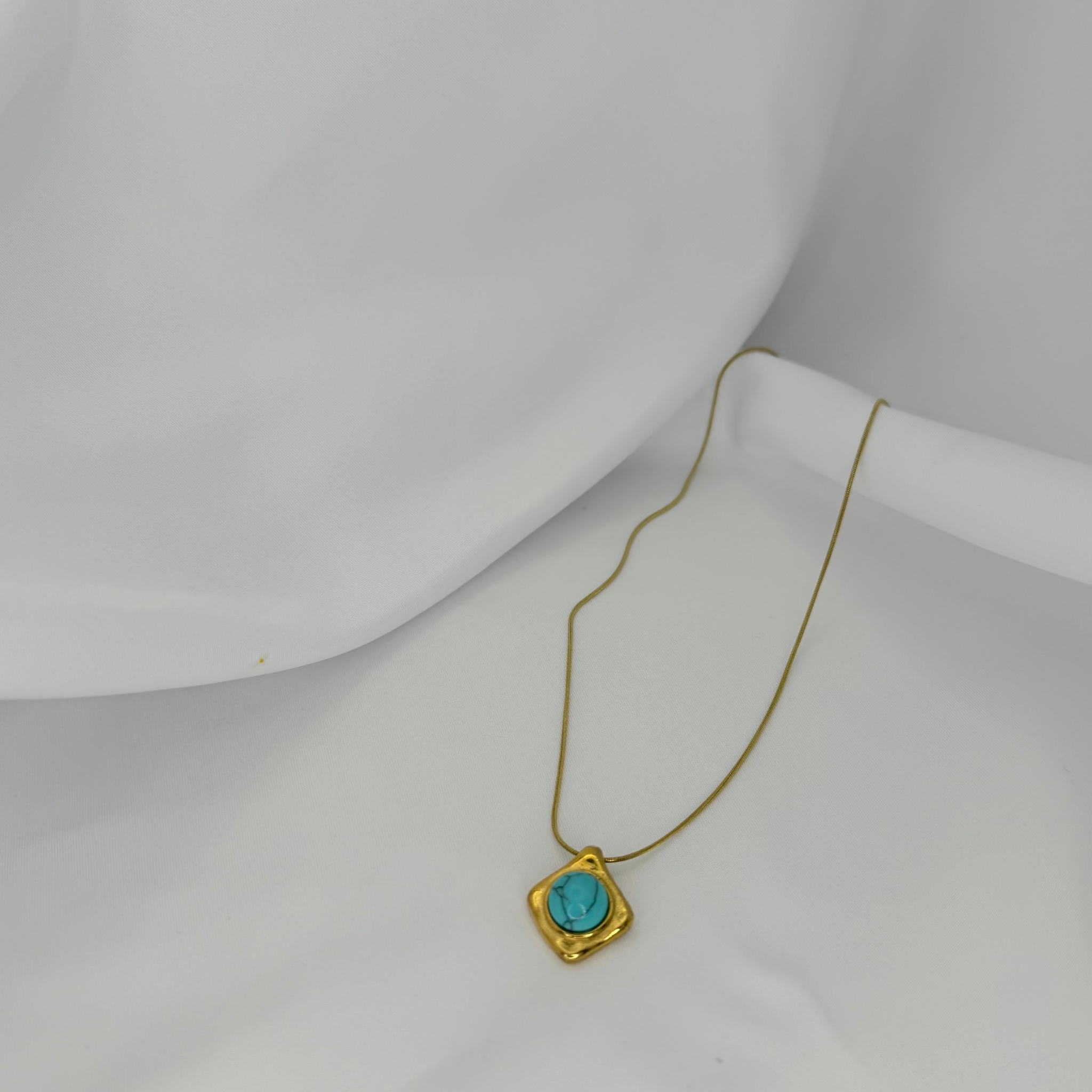 Gold necklace with a turquoise pendant on a white mannequin bust.