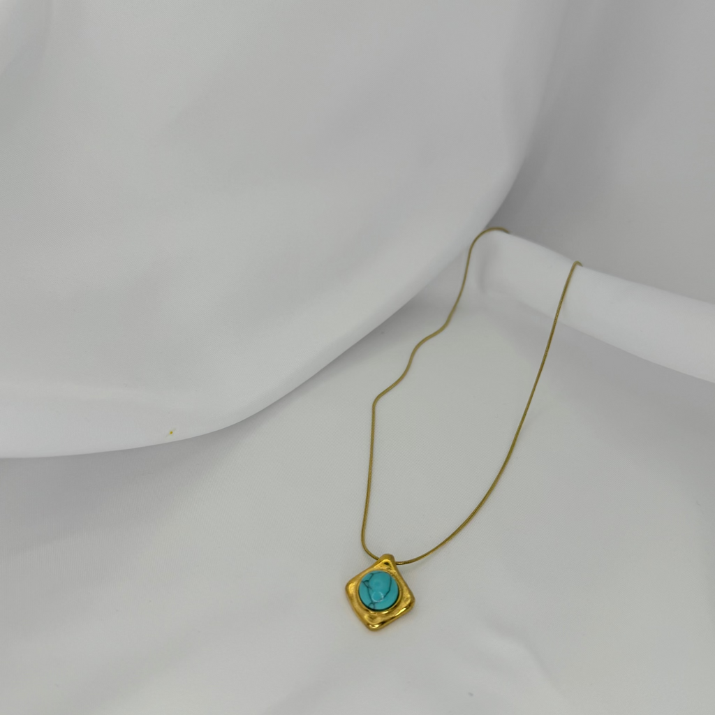 Gold necklace with a turquoise pendant on a white mannequin bust.