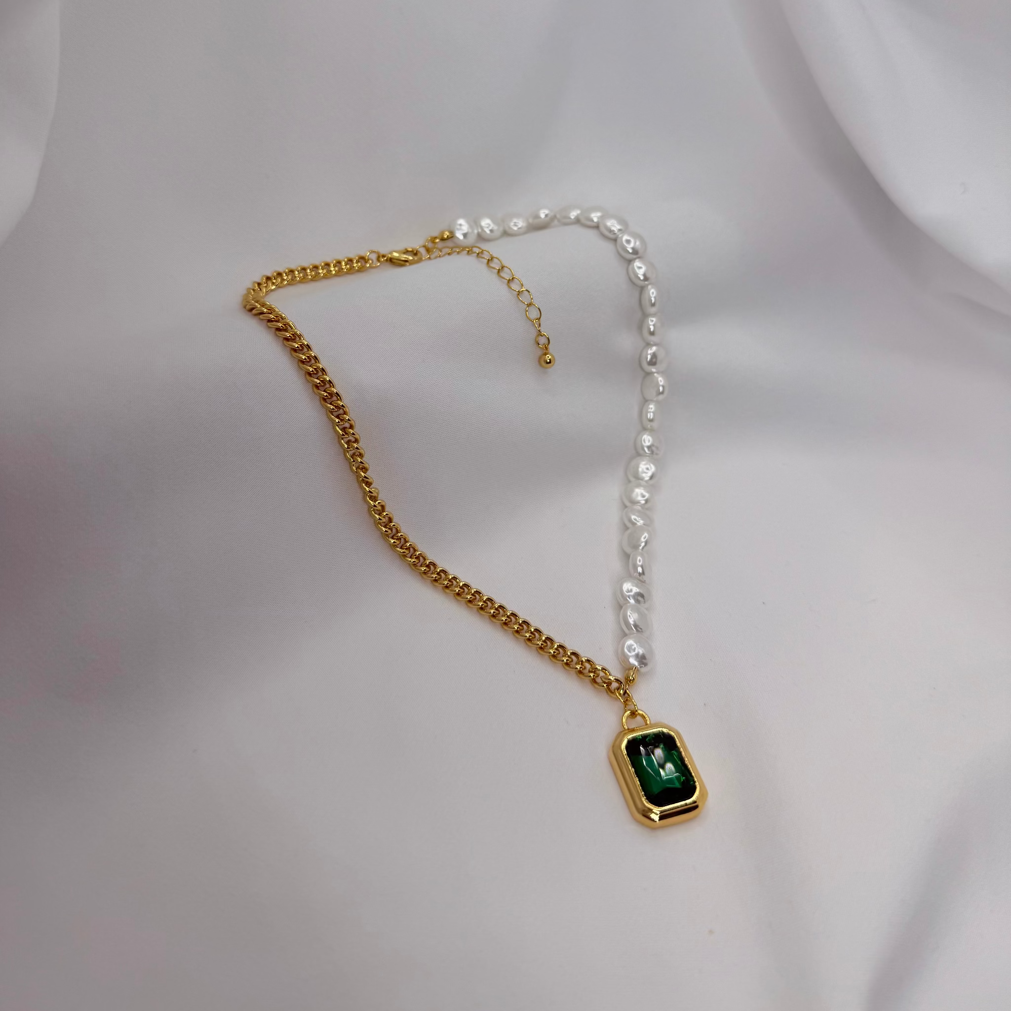 Gold and silver chain necklace with a green gemstone pendant on a white fabric background