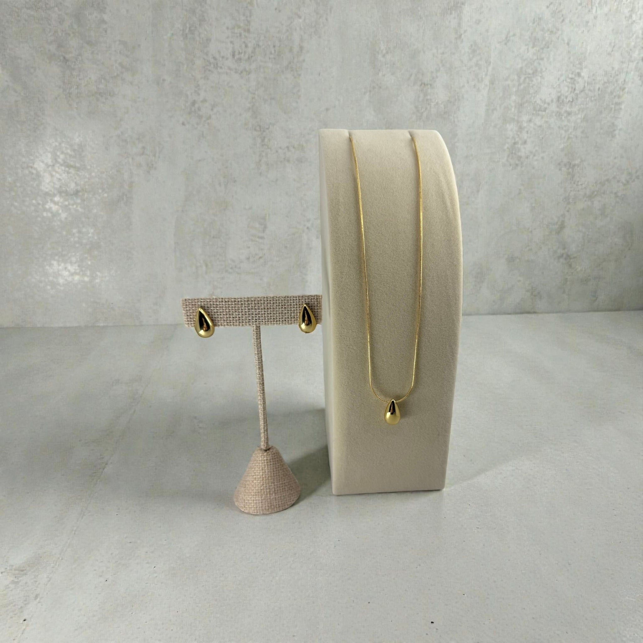 Gold necklace and earrings on a gray surface with a neutral background