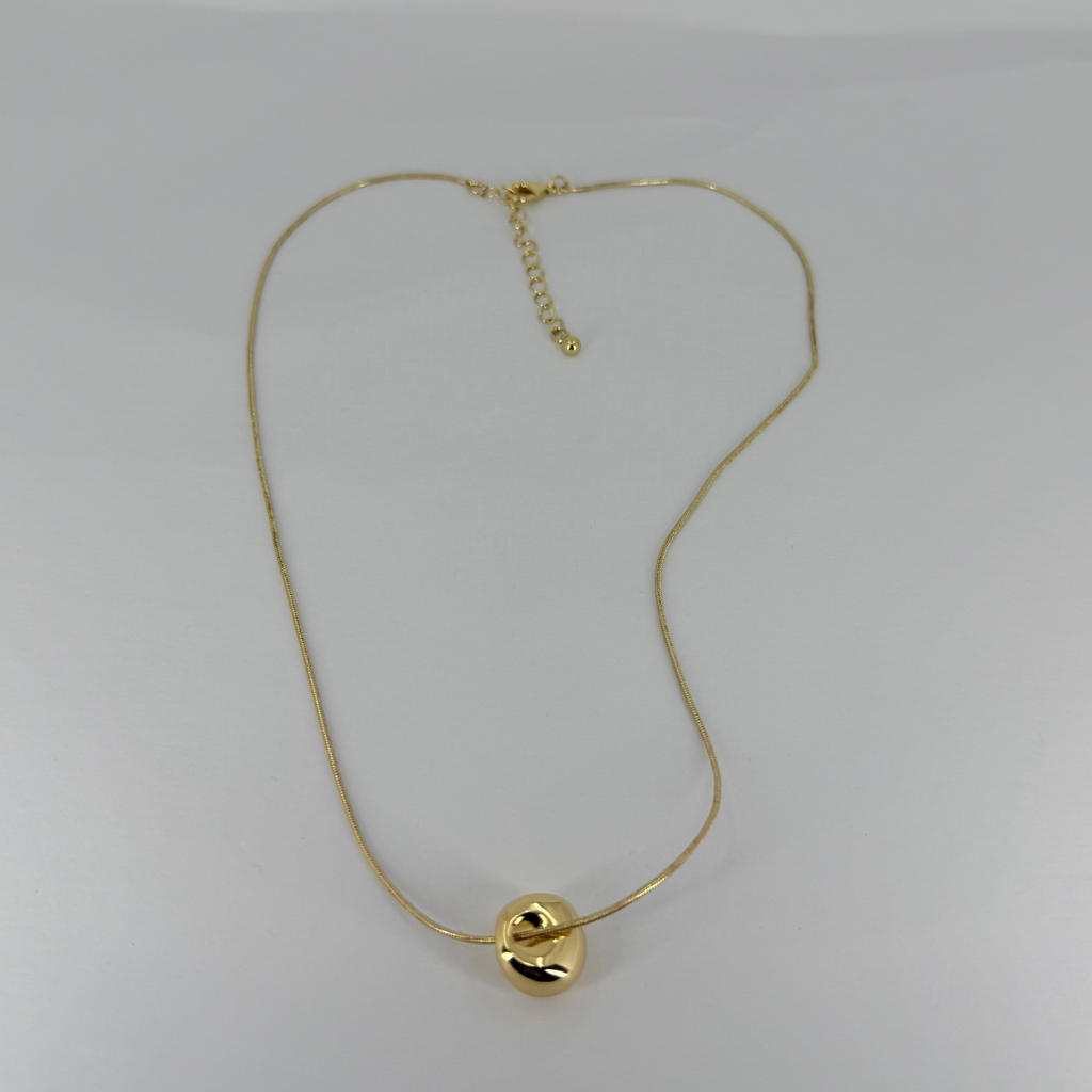 Gold necklace with a small round pendant on a light gray background
