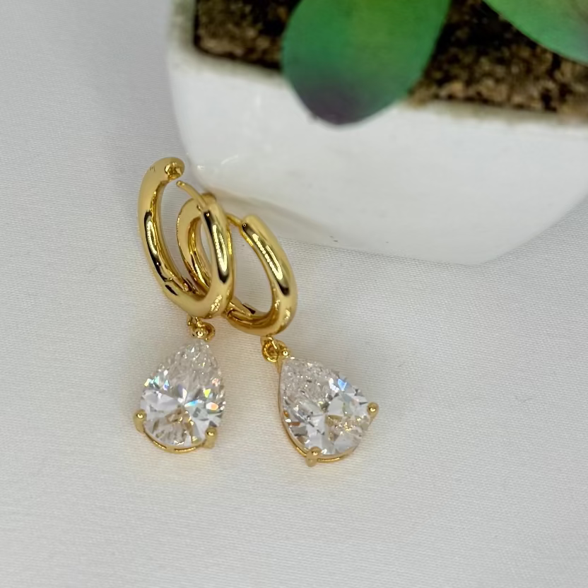 Gold earrings with clear stones on a white surface with a small potted succulent.
