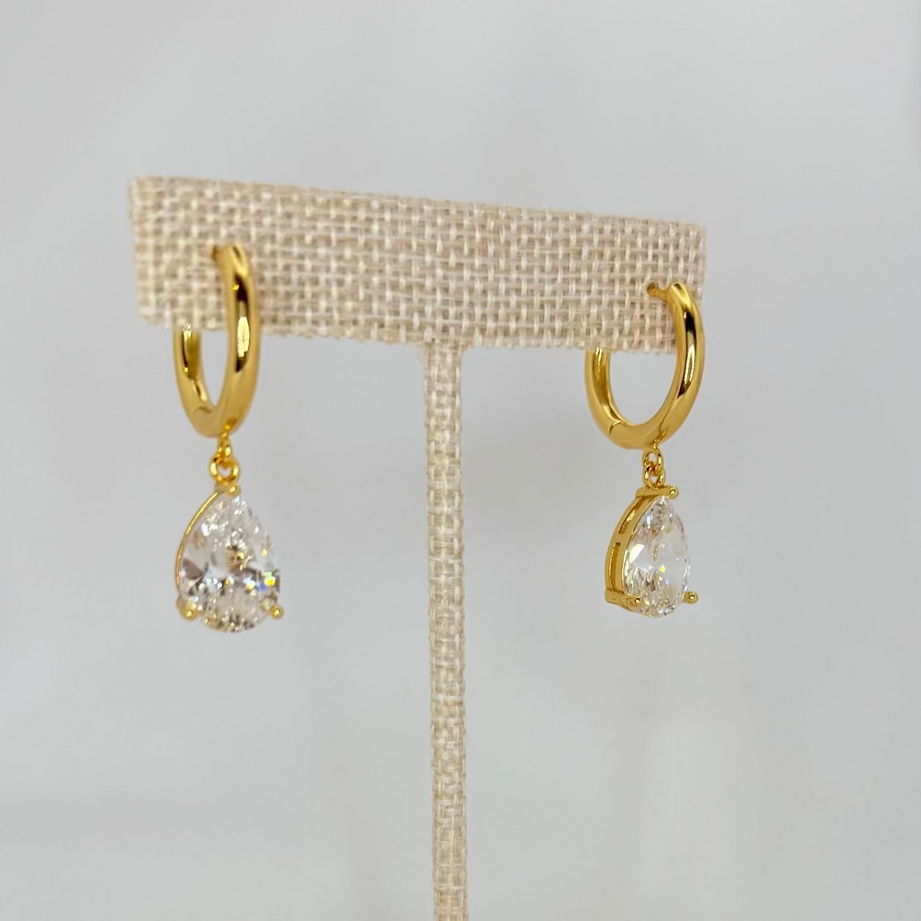 Gold earrings on a beige earring stand against a white background