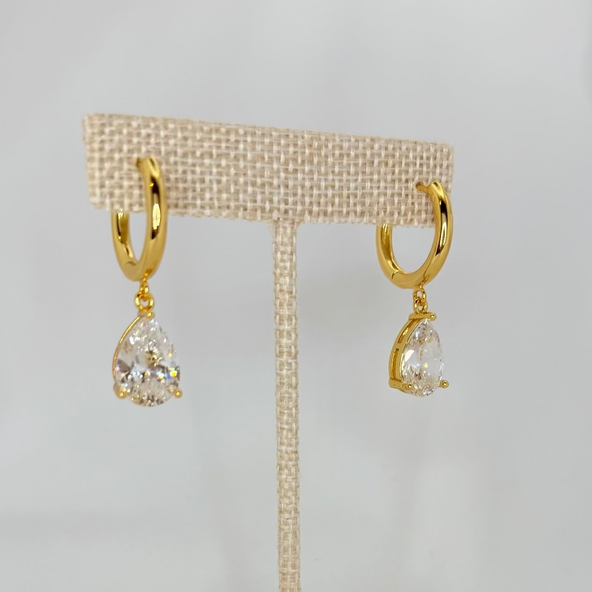 Gold earrings on a beige earring stand against a white background