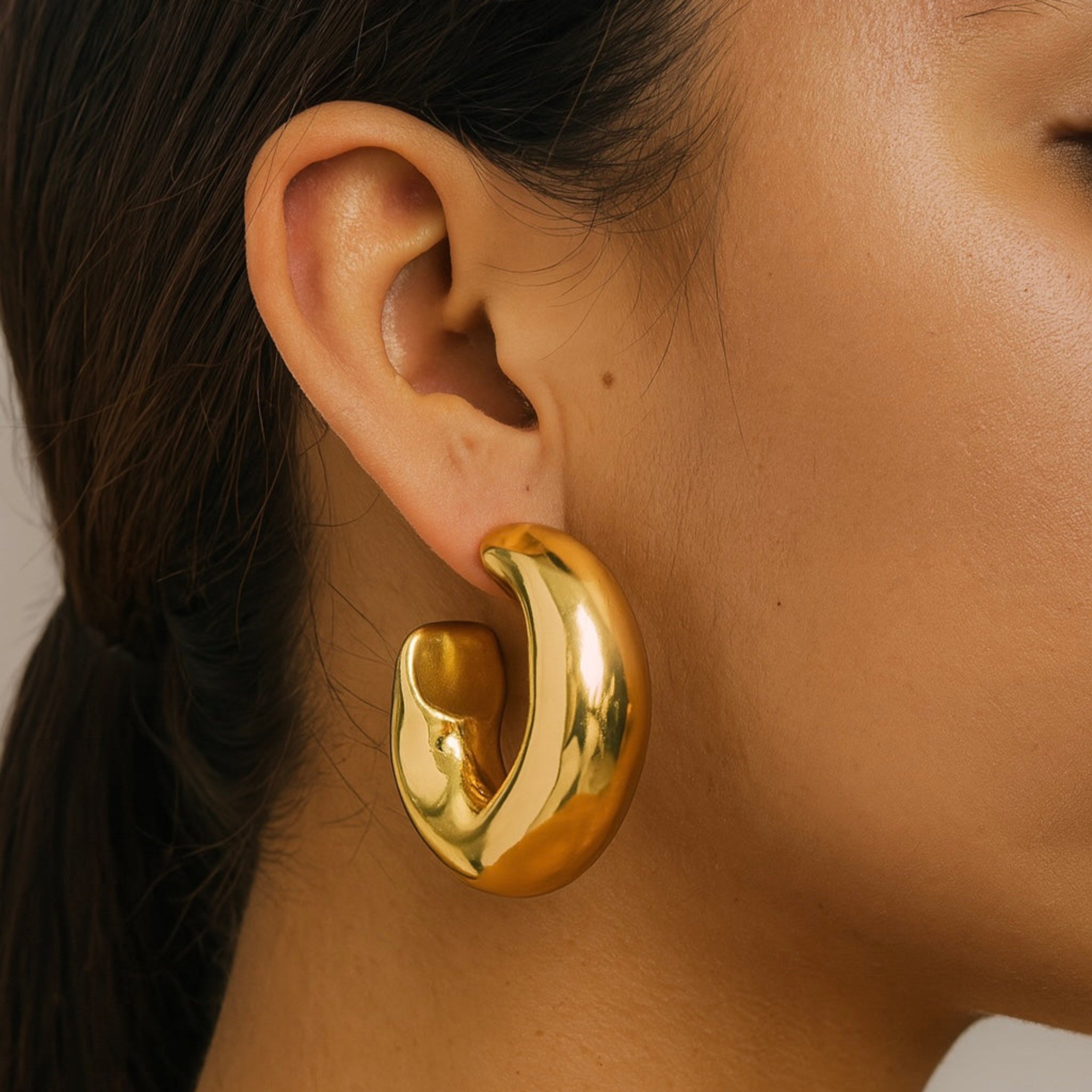 Gold hoop earring worn by a person with a neutral background