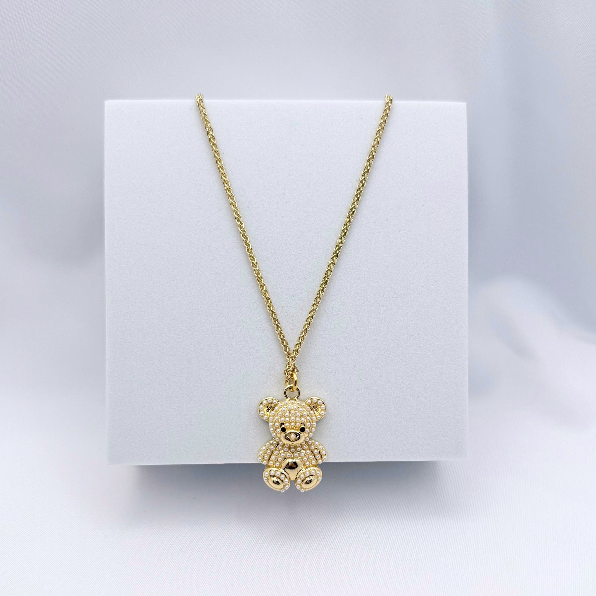 Gold teddy bear necklace on a white card with a light gray background