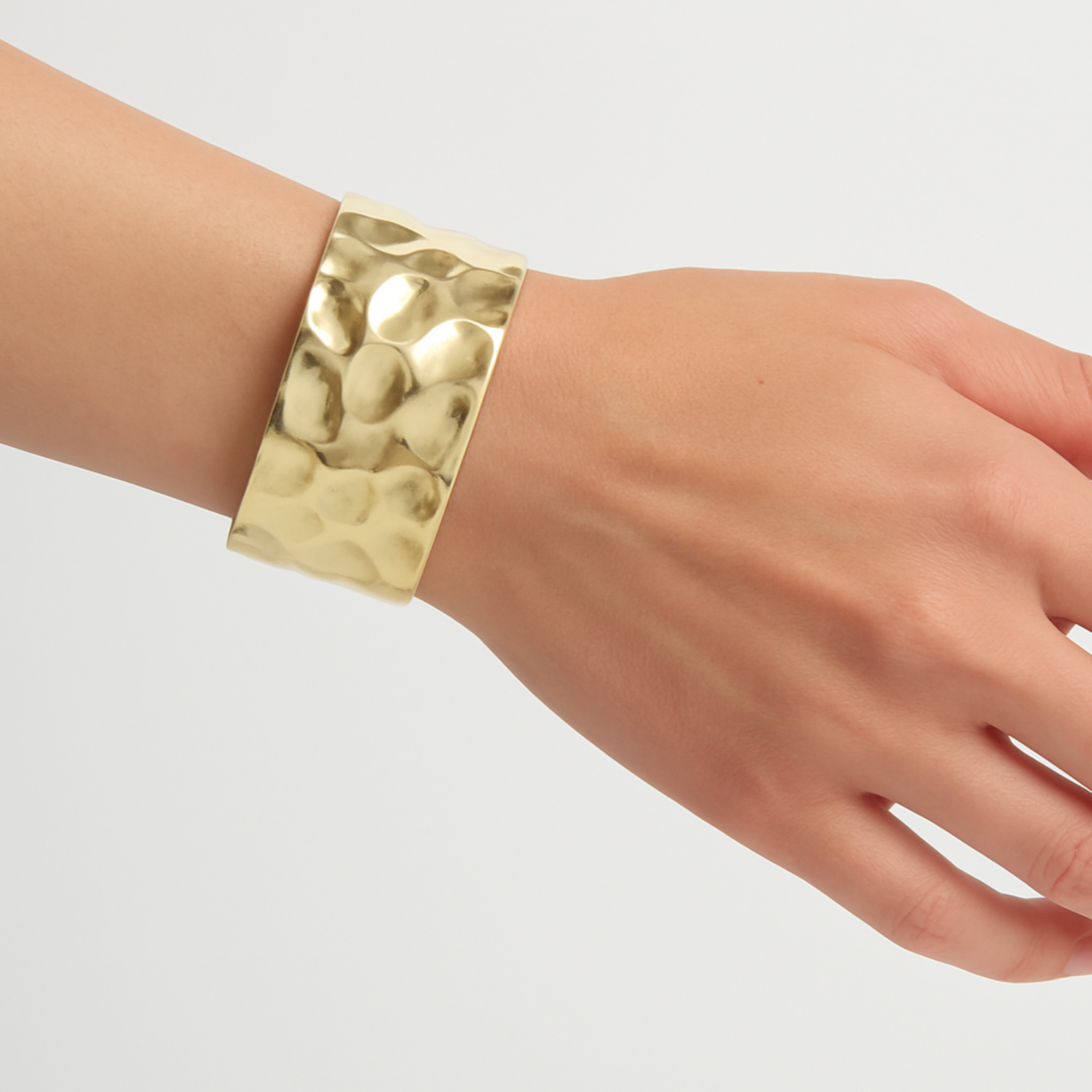 Gold bracelet on a wrist against a plain background