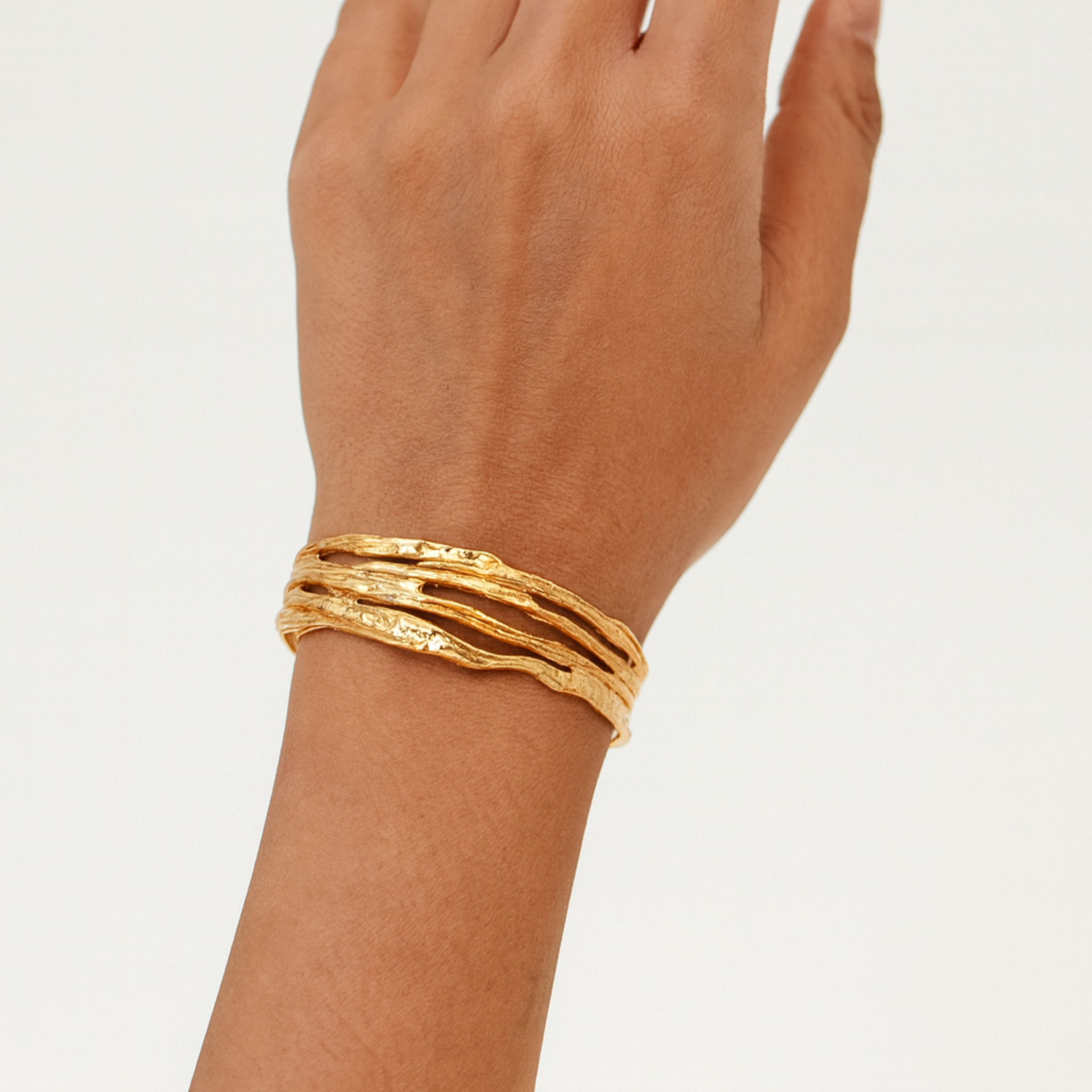 Gold bracelet on a hand against a plain background