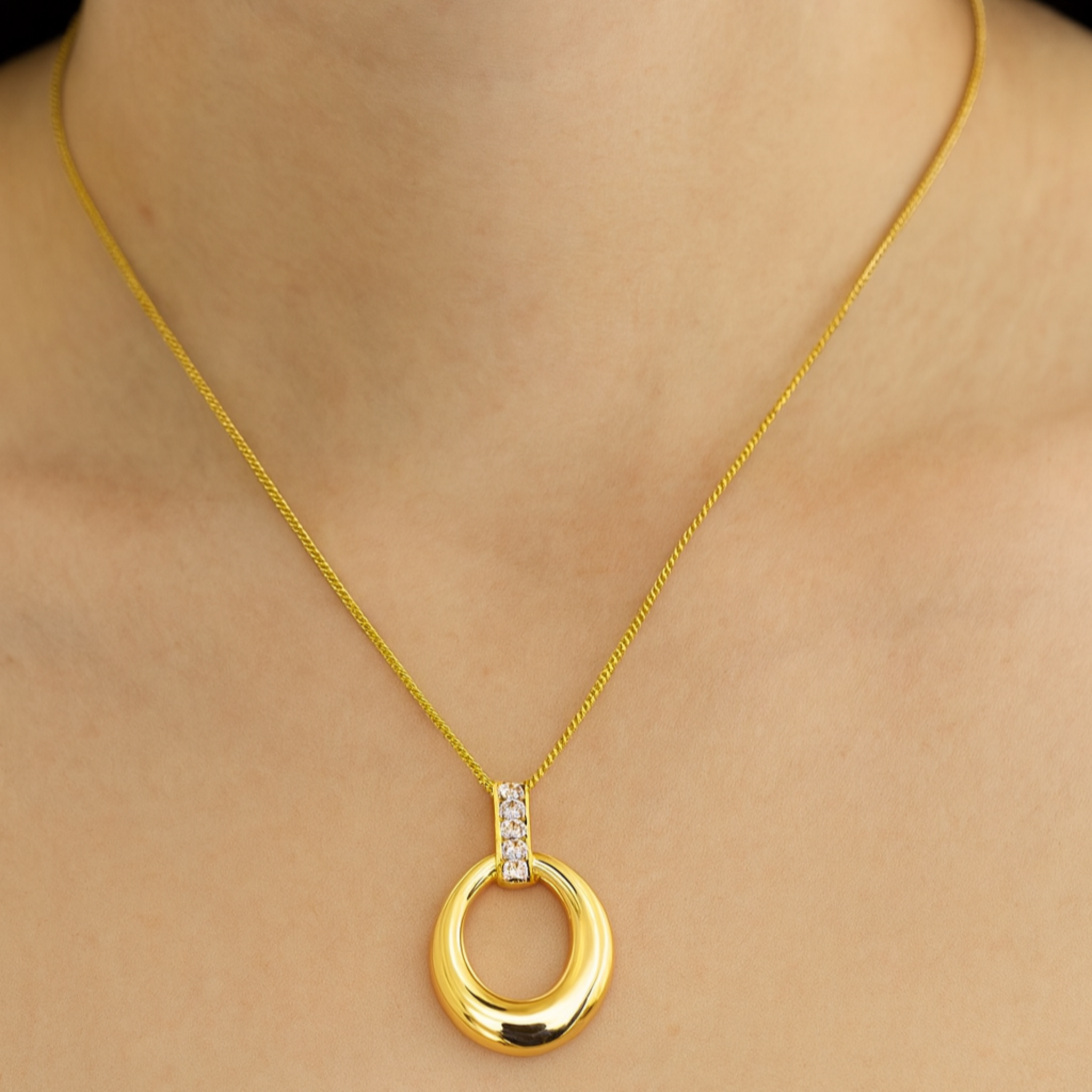 Gold necklace with a circular pendant on a person wearing a white top.