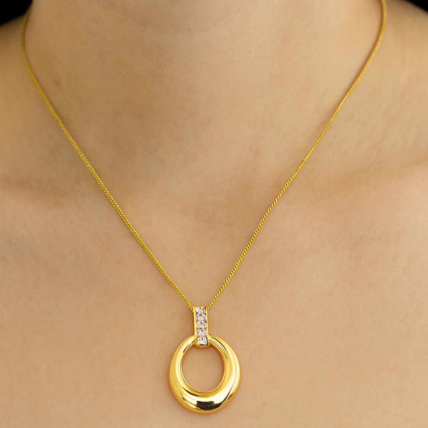Gold necklace with a circular pendant on a person wearing a white top.