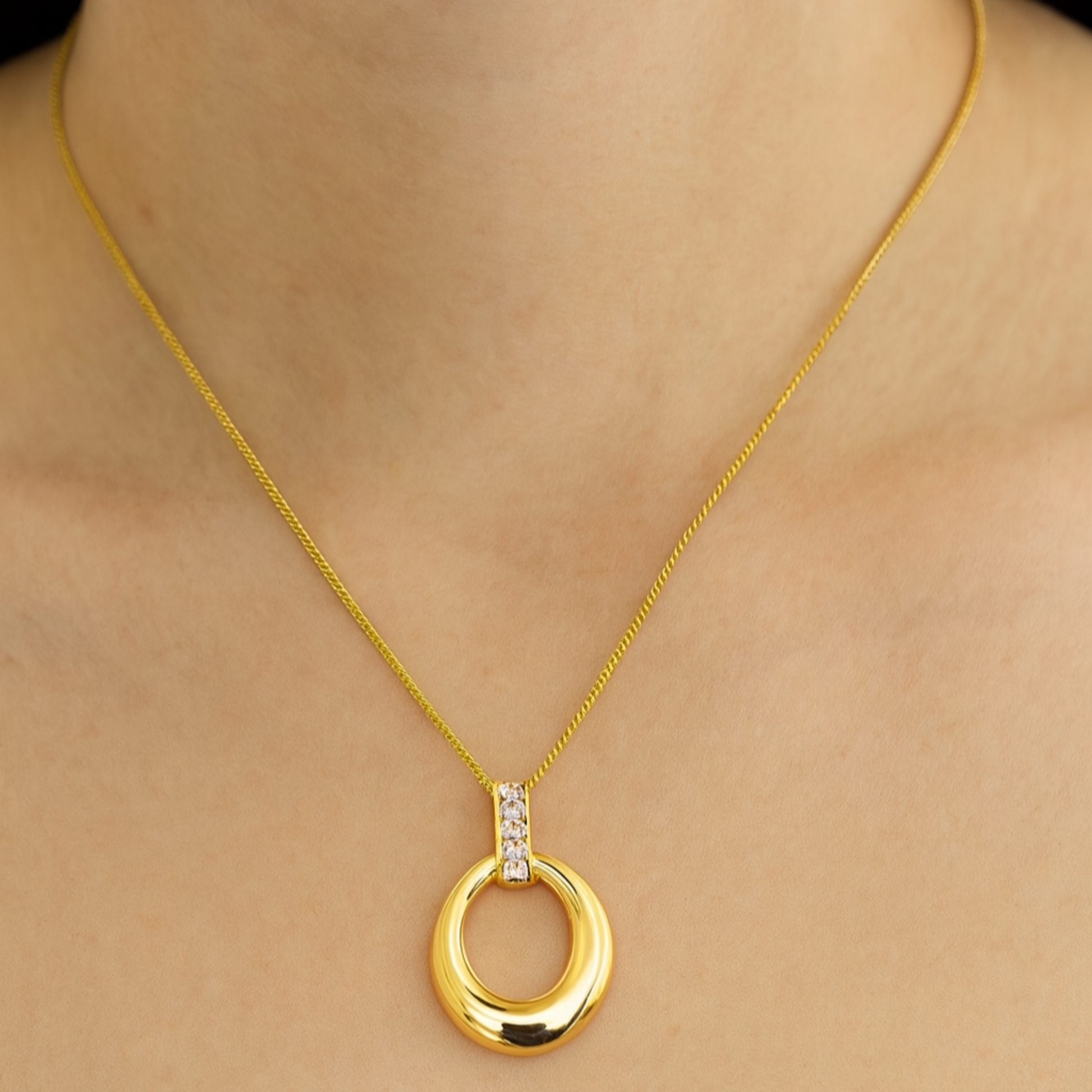 Gold necklace with a circular pendant on a person wearing a white top.