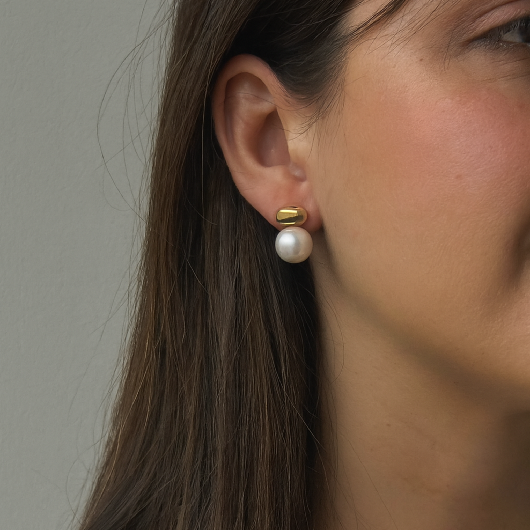 Close-up of a person wearing pearl earrings with a neutral background