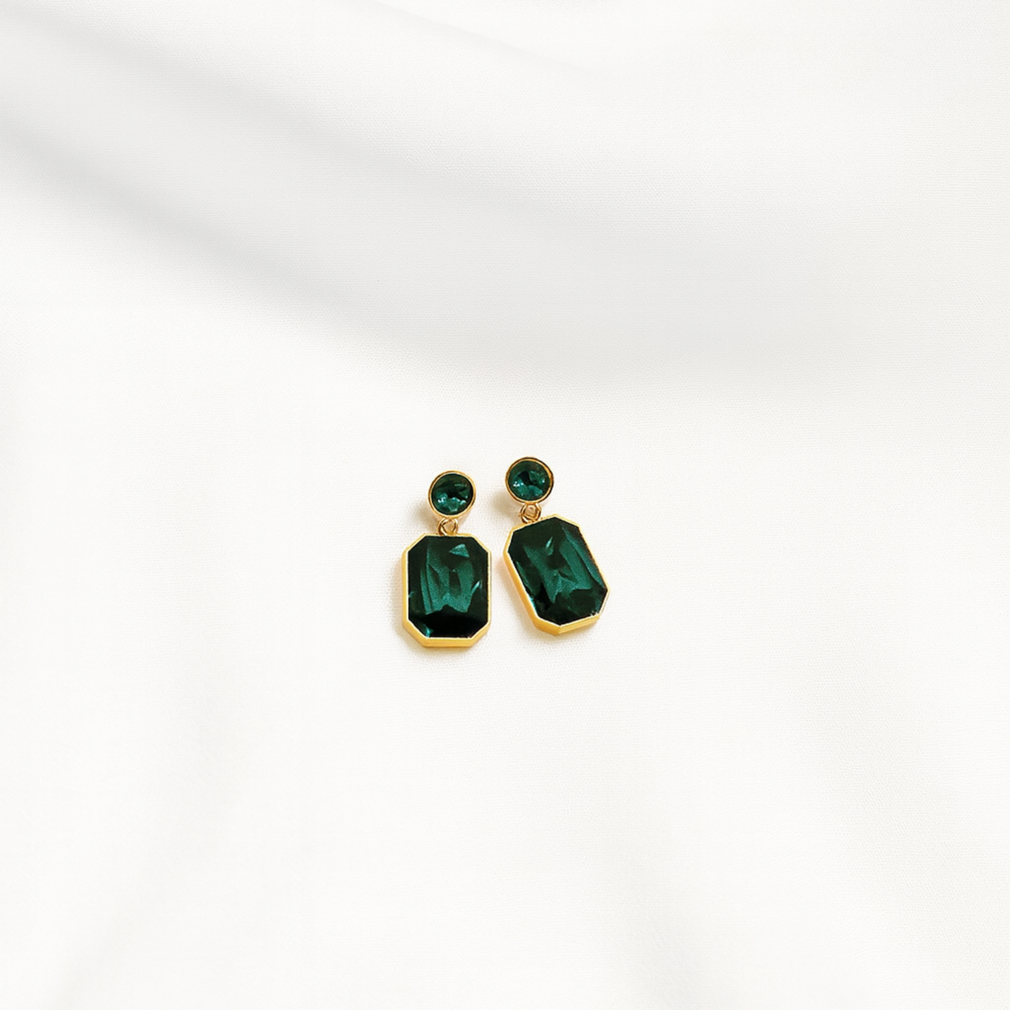 Gold earrings with green gemstones on a white background