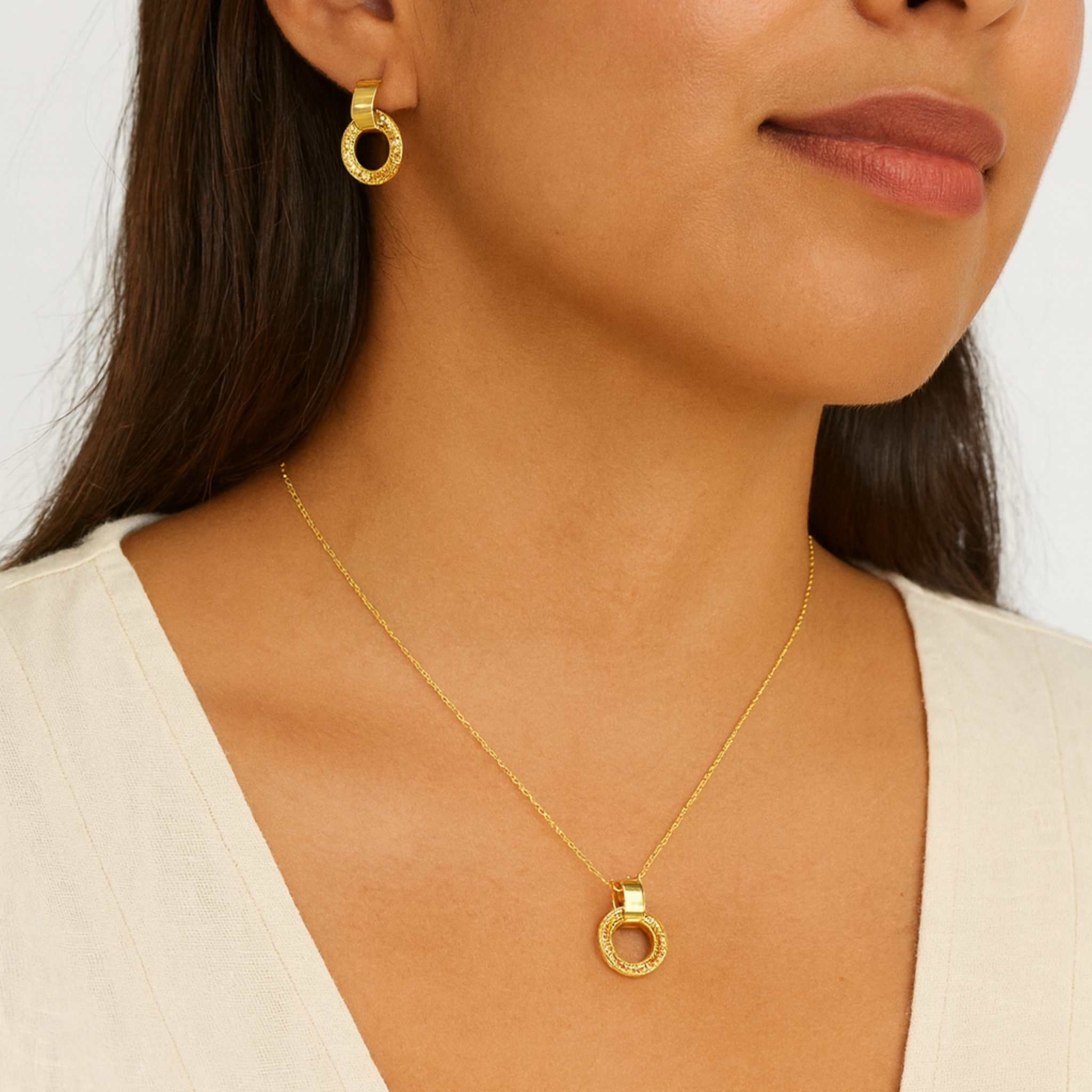 Woman wearing gold earrings and necklace against a white background