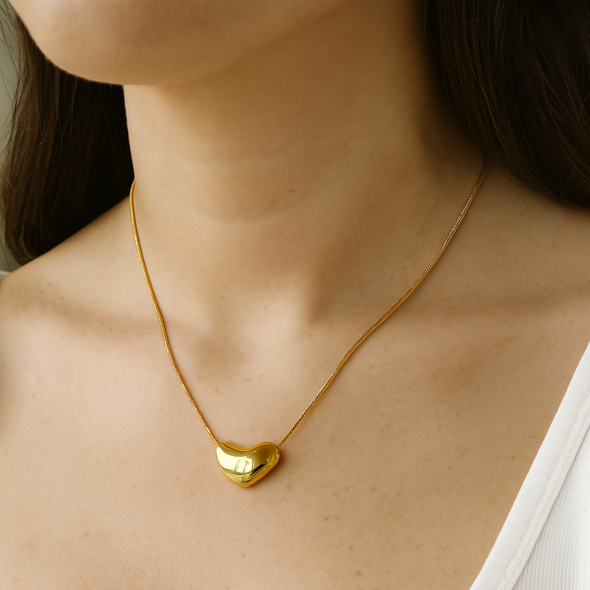 Gold heart-shaped necklace on a person wearing a white top