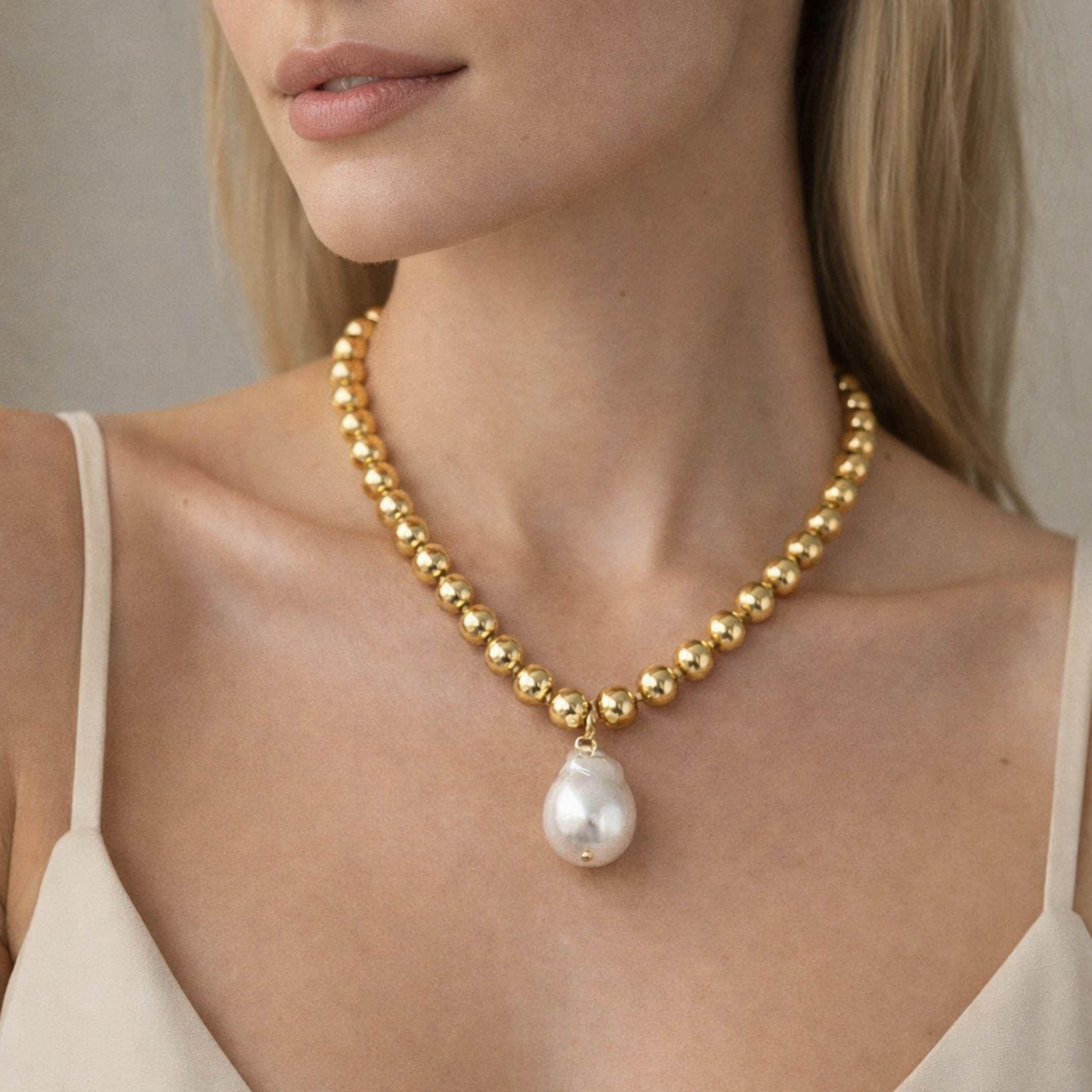 Woman wearing a gold necklace with a pearl pendant against a neutral background