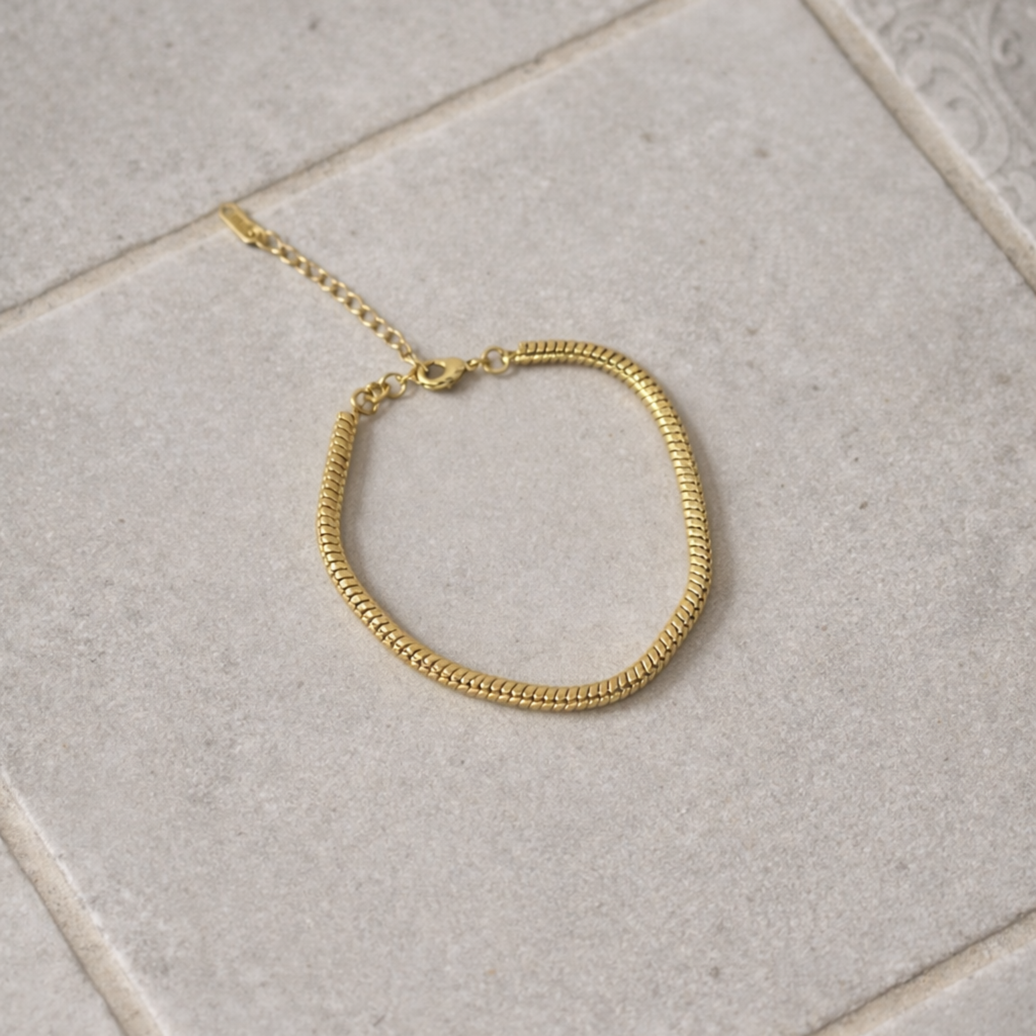 Gold bracelet on a light gray tiled floor