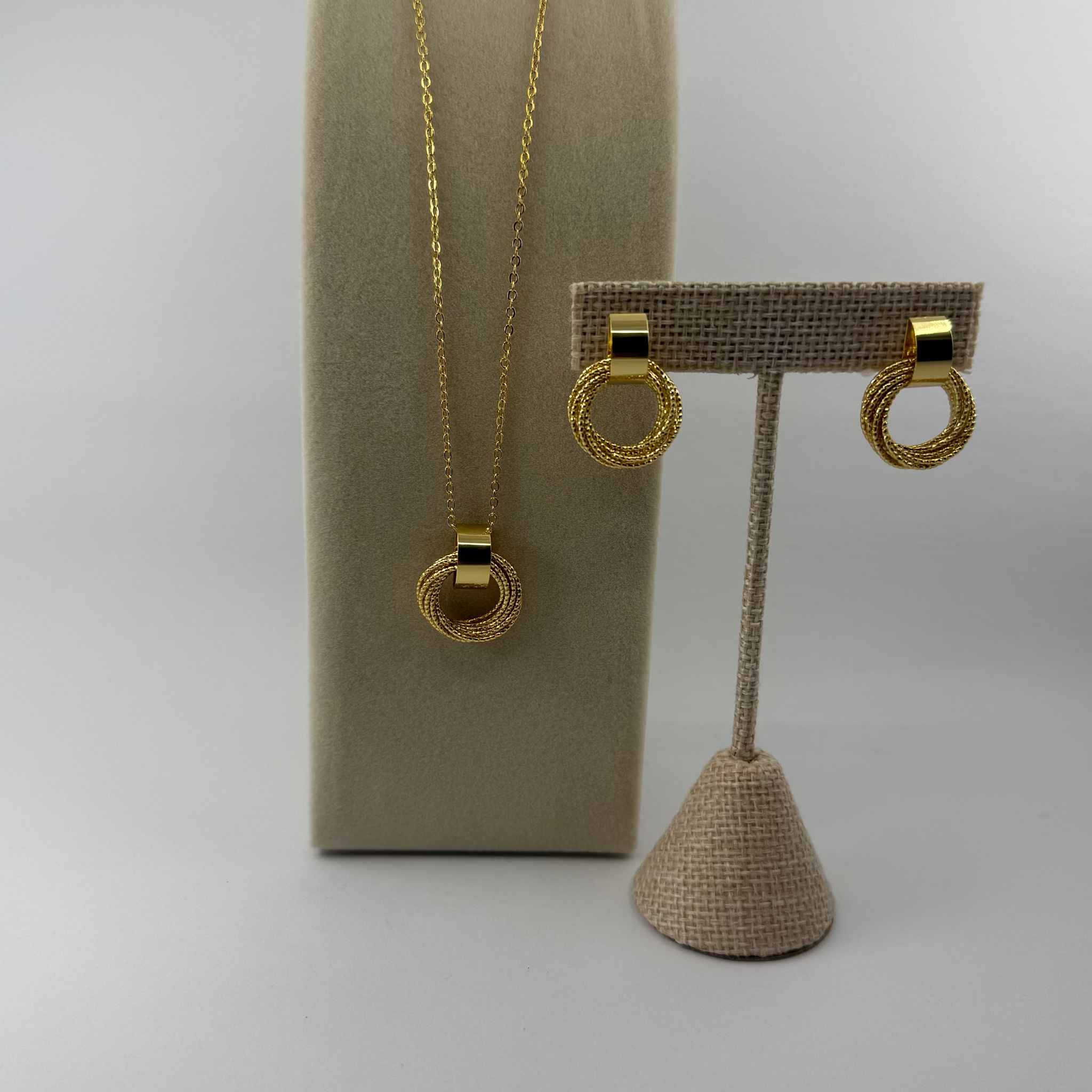 Gold necklace and earrings on a beige stand against a light gray background