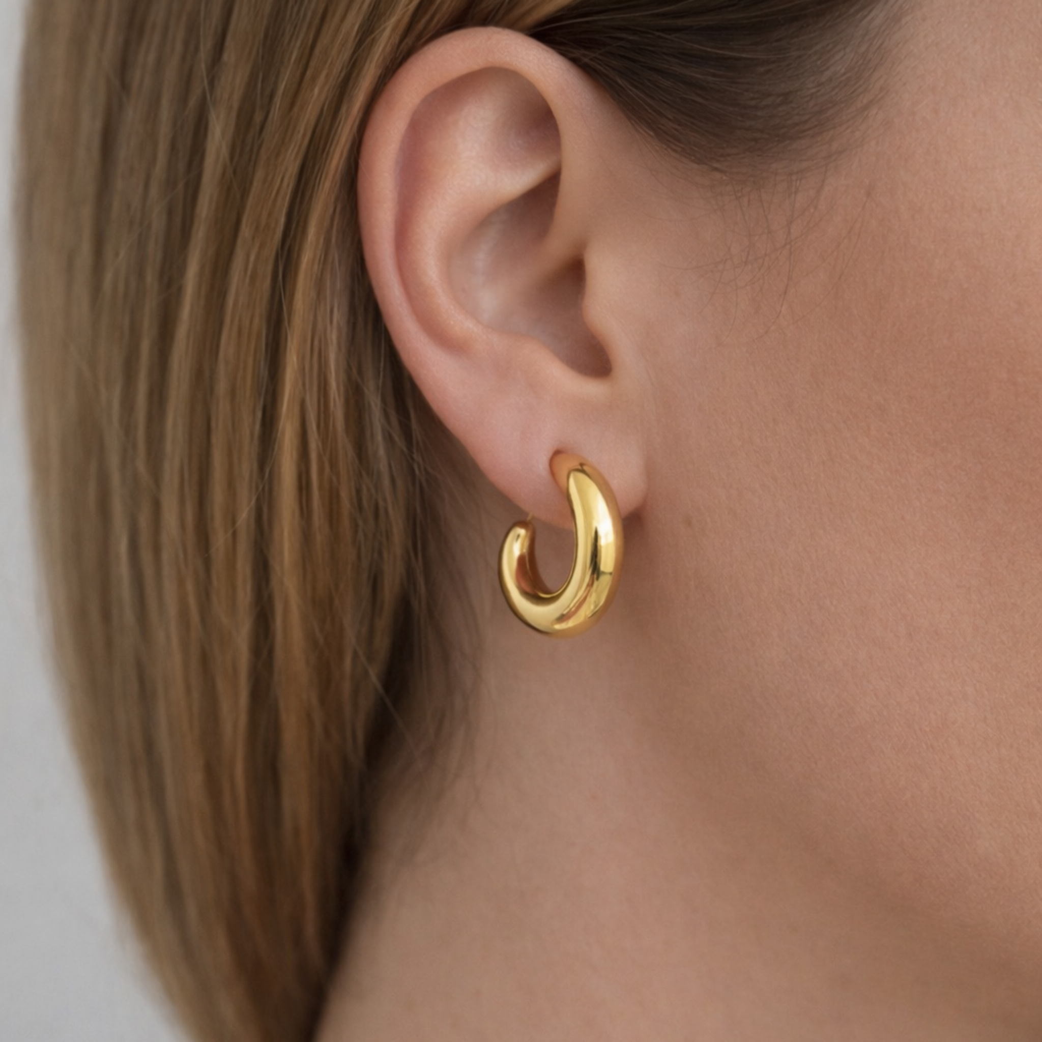 Gold hoop earring worn by a person with a neutral background