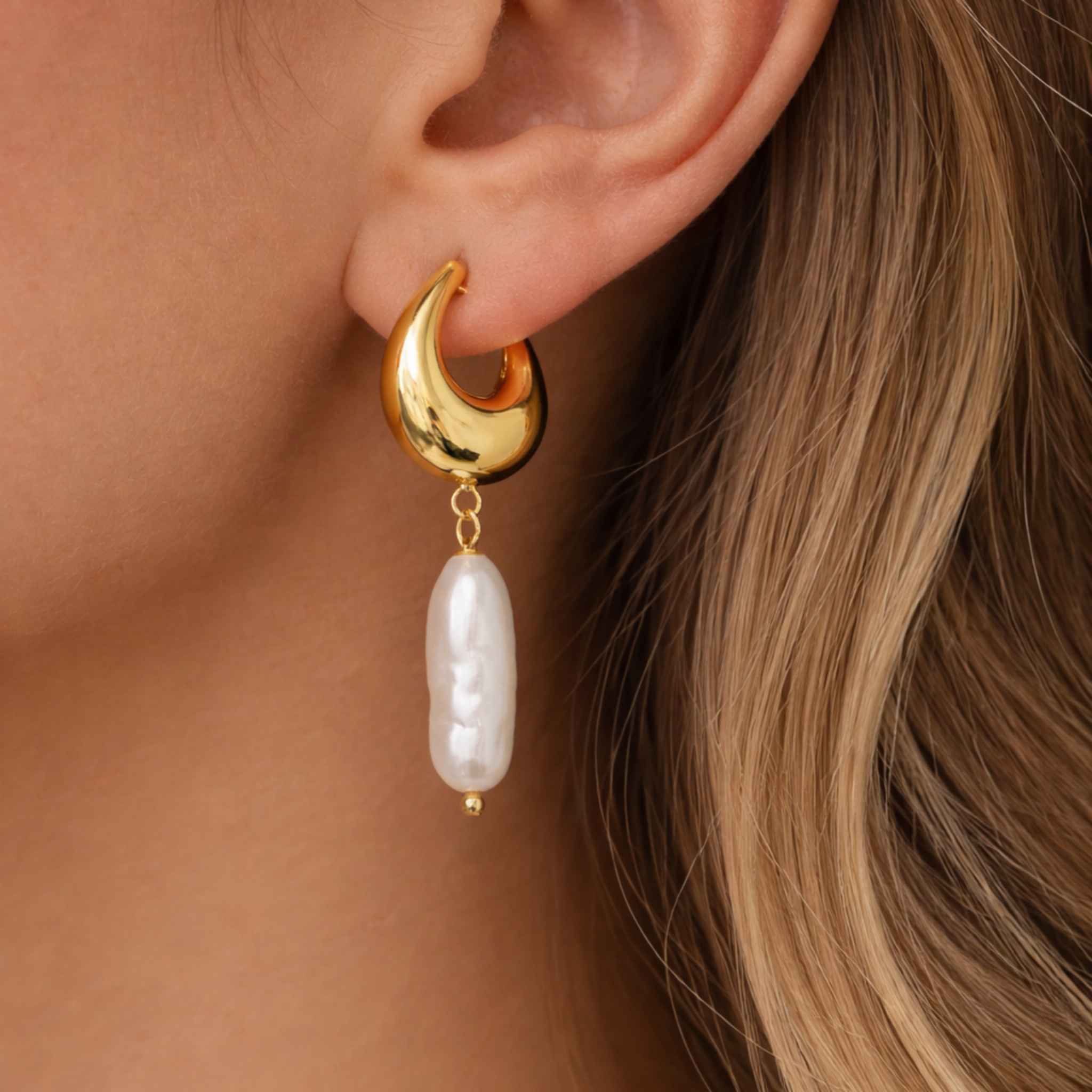 Gold earring with a pearl drop worn by a person