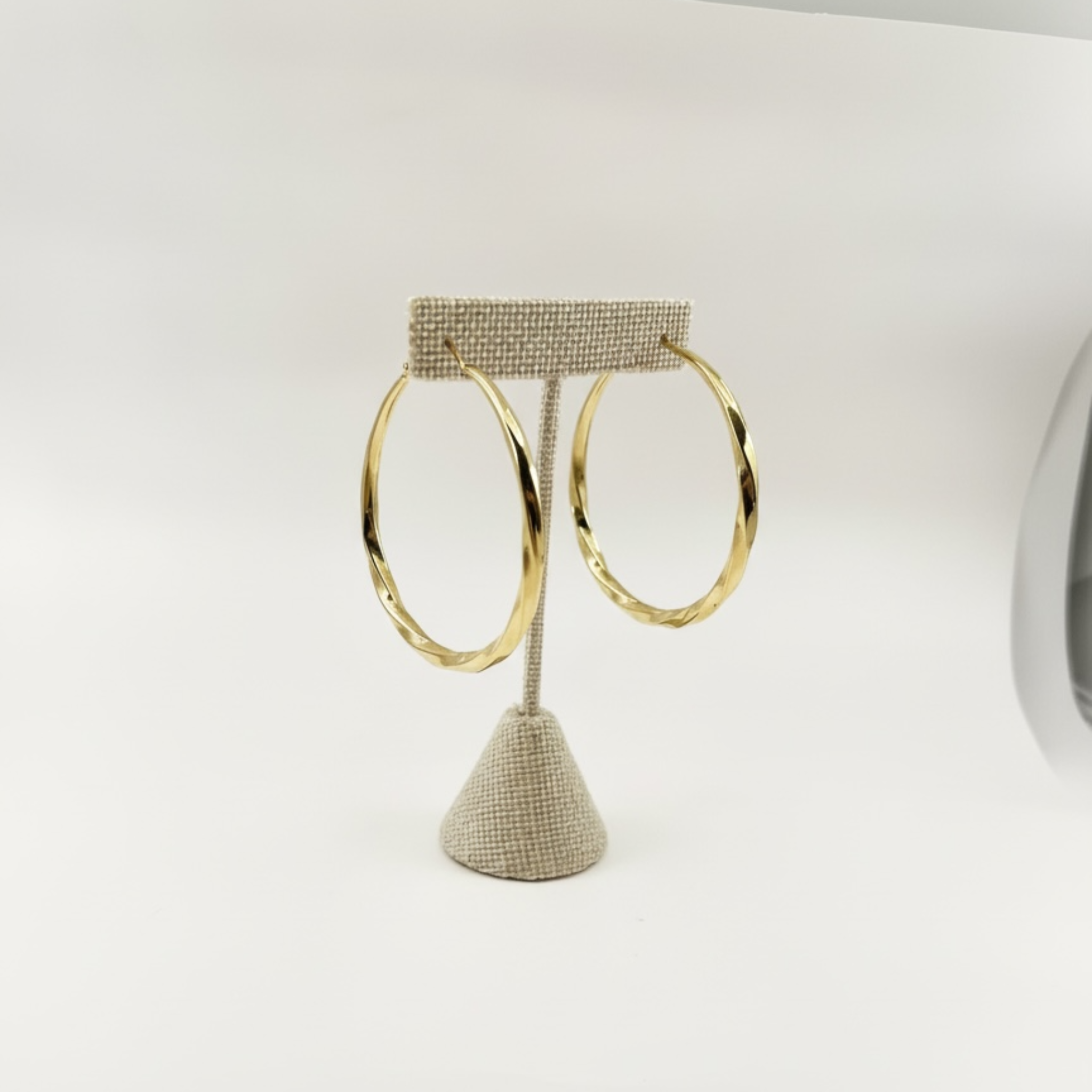 Gold hoop earrings on a textured stand against a white background